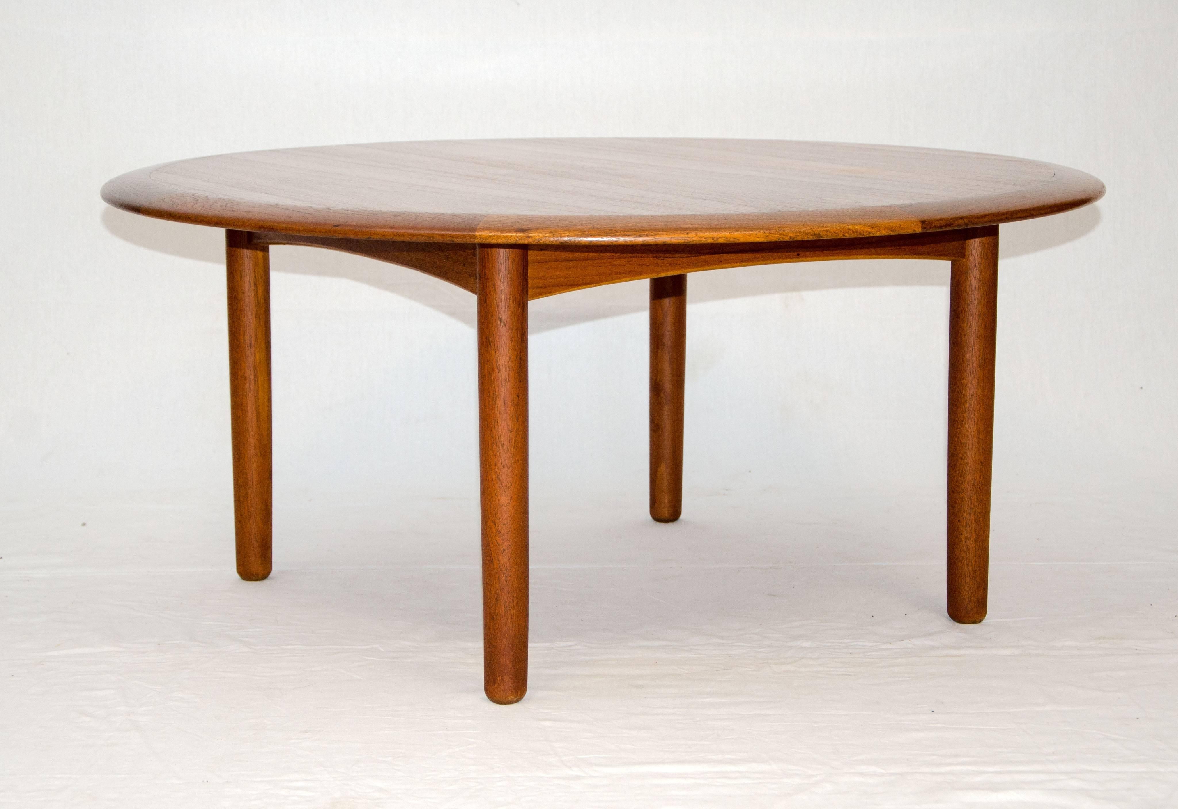 Simple well made Danish teak circular coffee table on round legs and accented by an opposite grain pattern border around the edge of the tabletop. Retains the manufacturer stamp and a Danish control tag.