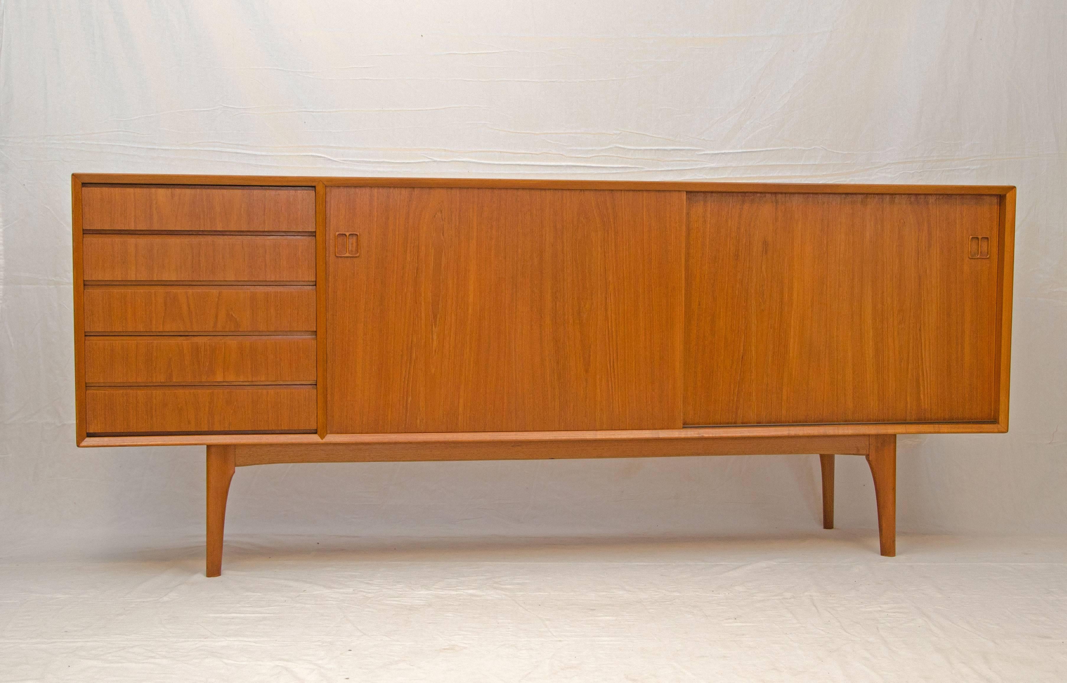 Danish teak credenza with two sliding doors and five storage drawers. The top drawer is felt lined and also has another felt lined sliding half drawer. The shelves are adjustable. Drawer bottoms, sides and the cabinet interior and shelves are