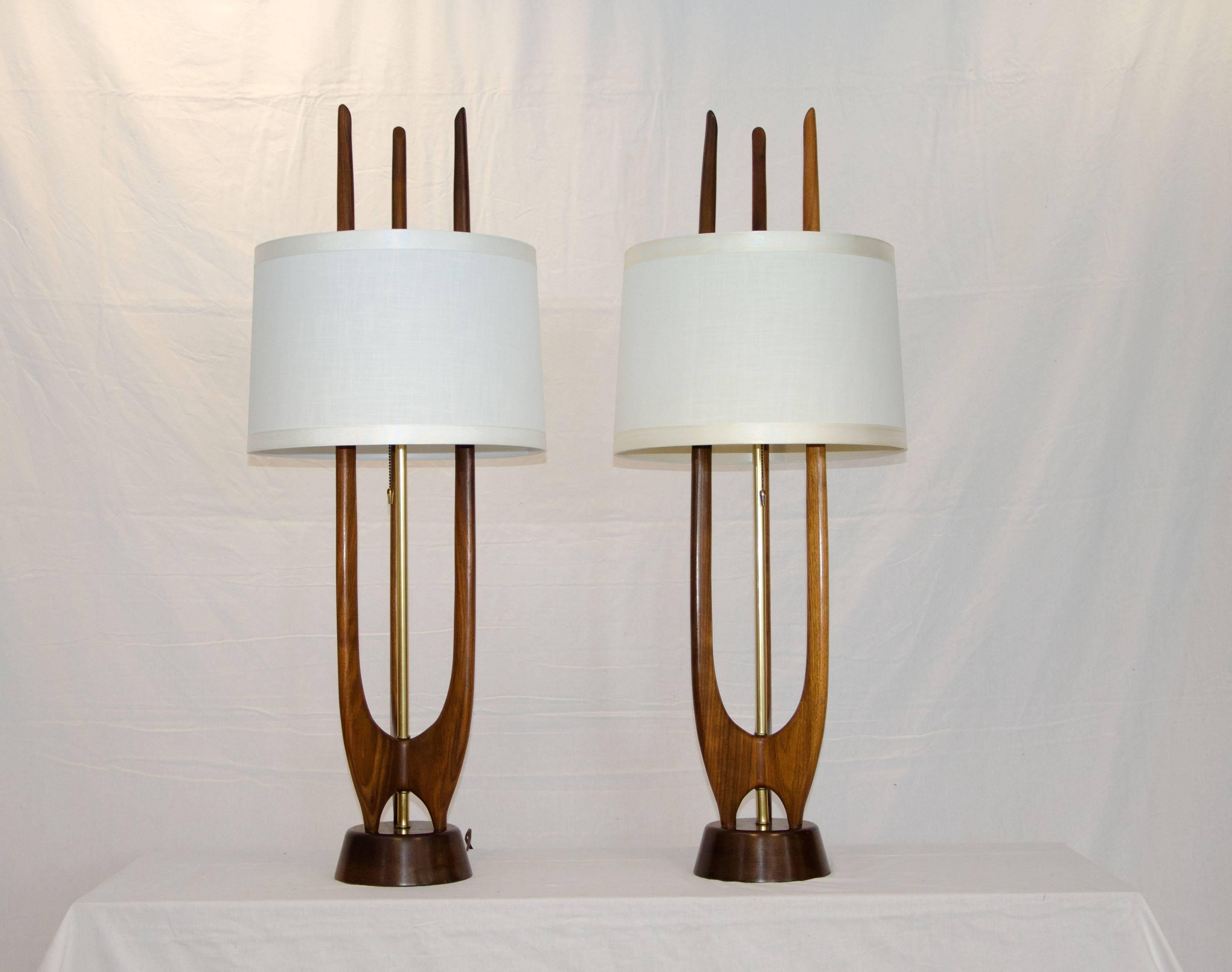 Very nice pair of walnut Modeline style table lamps. Three walnut prongs are attached to a circular base with a brass accent tube in the center. The lamps turn on and off with a pull chain with a small brass accent.