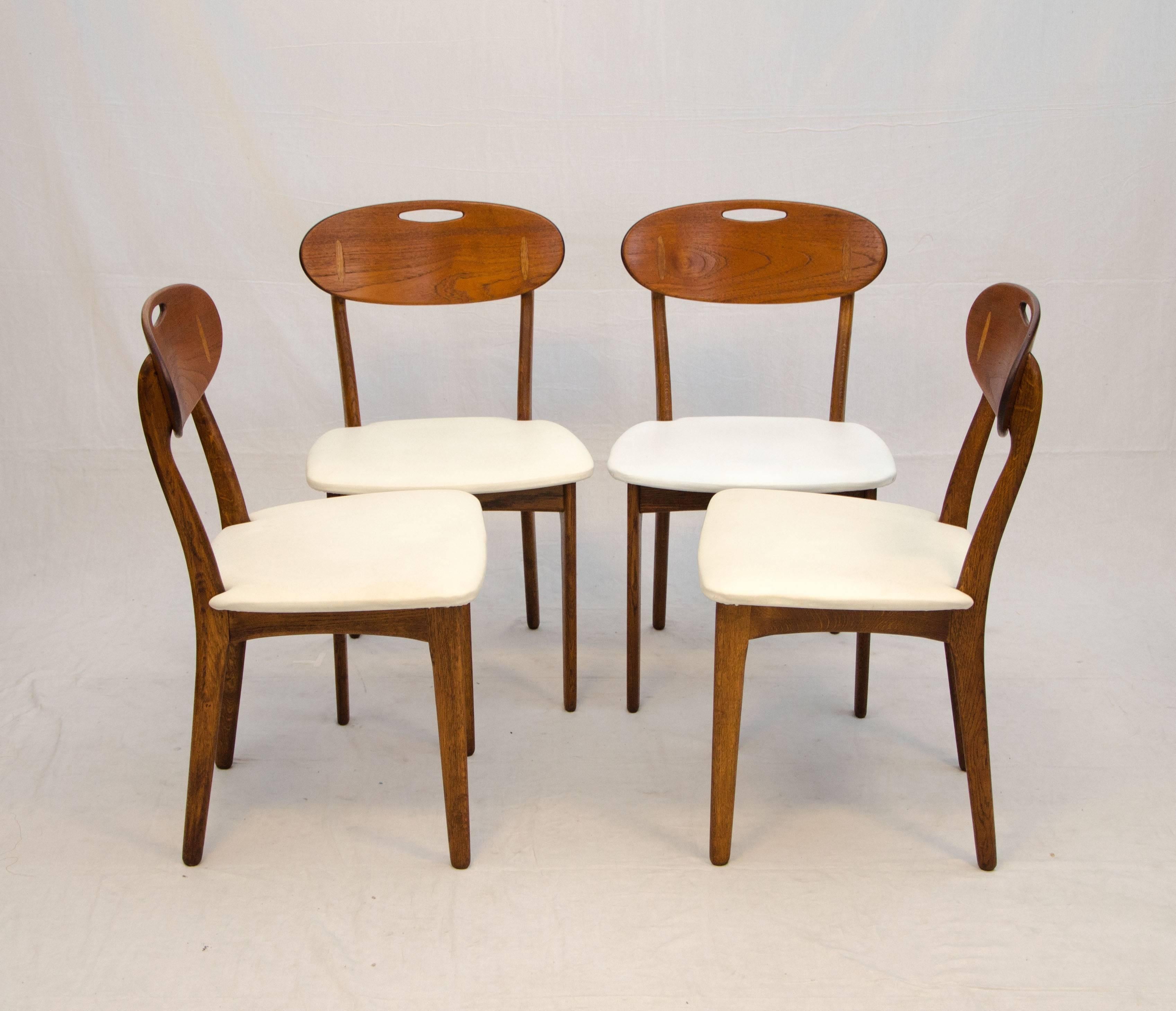 Comfortable and unusual design with a combination of wood types with teak backs, Hans Wegner style oak inserts, and oak chair frames. Retains designer and manufacturer's markings. These chairs are especially easy to move by using the cut-out handle