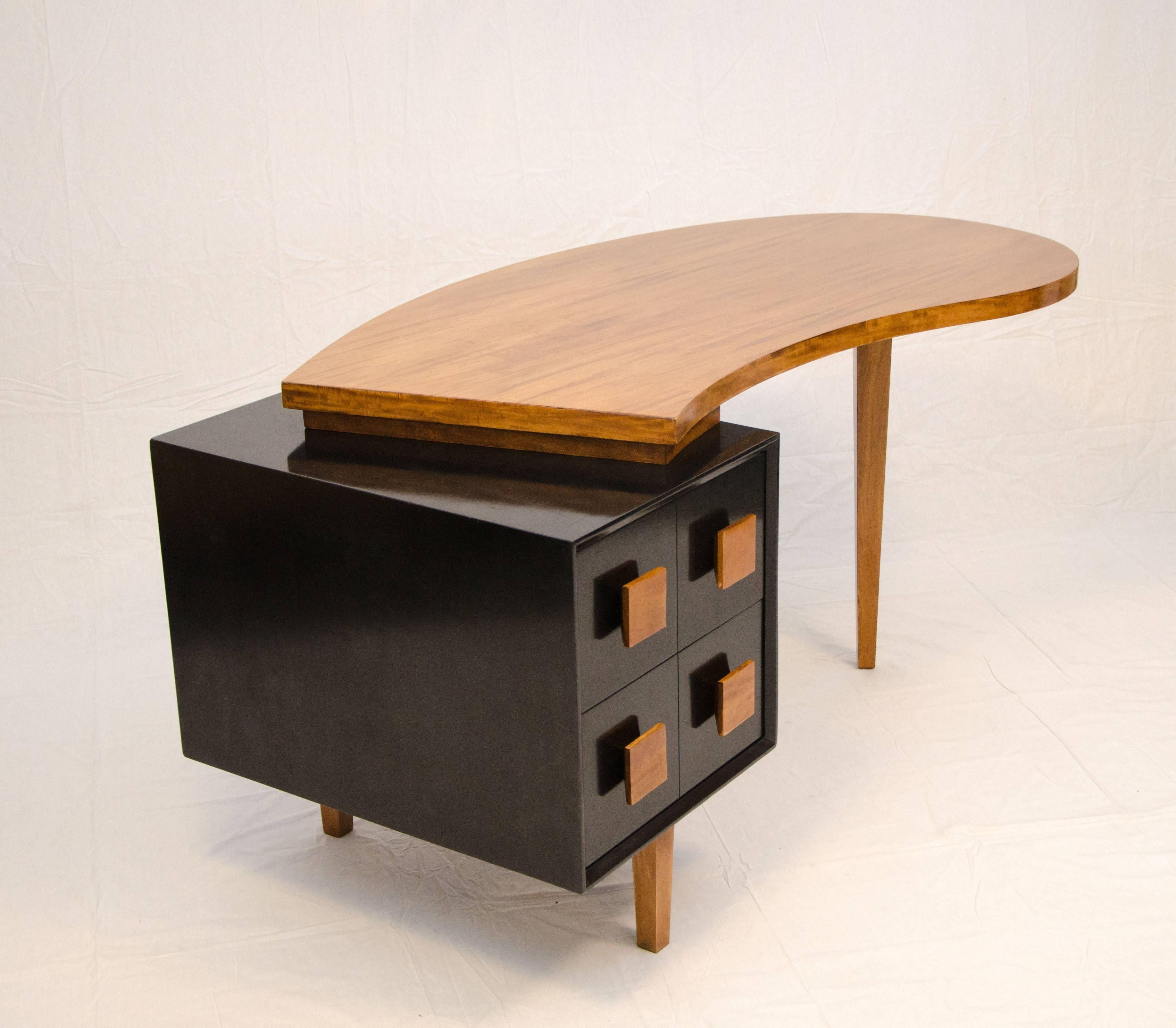 Nice American made desk with an organic semi kidney shaped top offset and a satin black lacquered drawer cabinet. The two drawers are accented by square wooded pulls matching in color with the top surface. It would look great in the centre of a toom