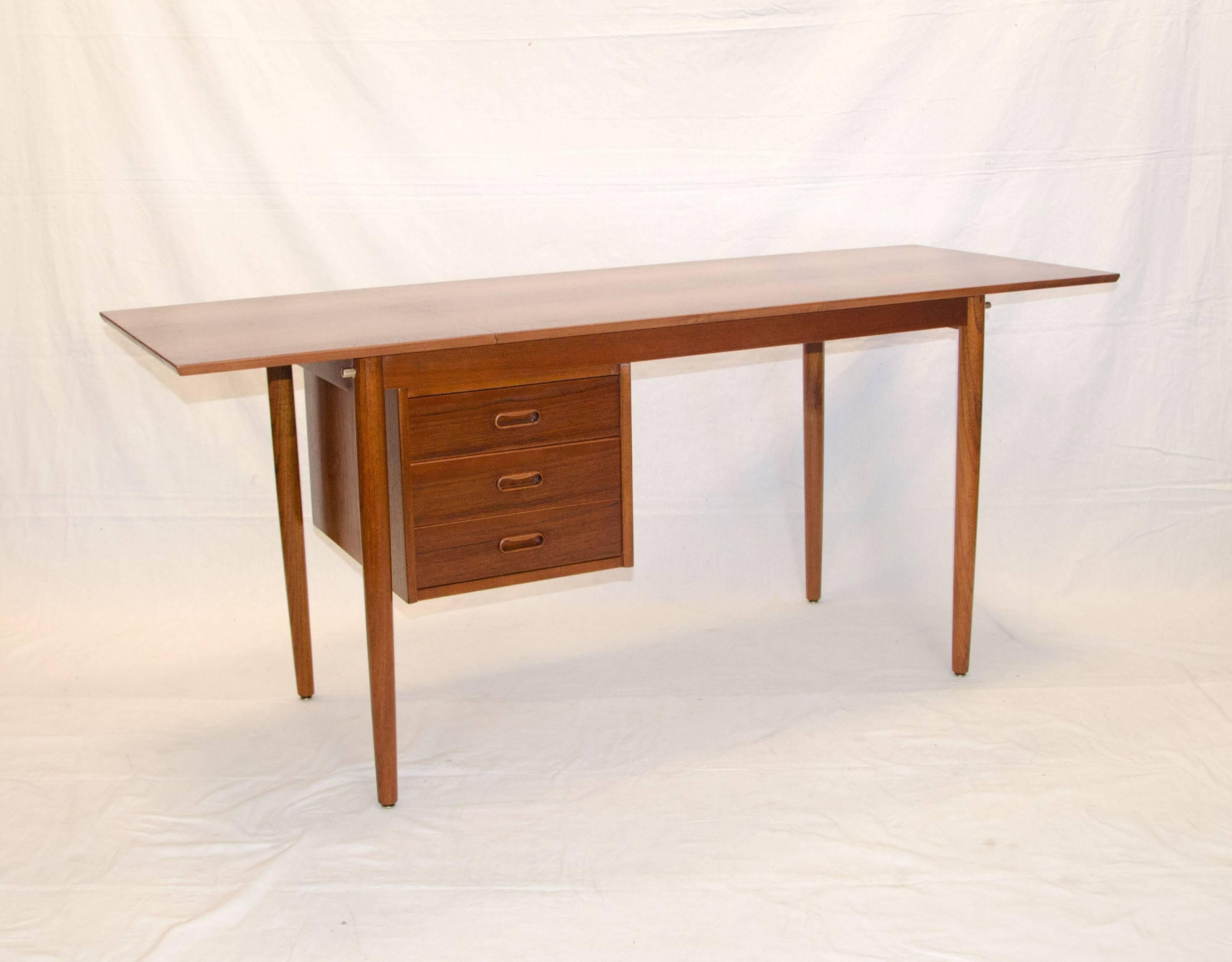 This medium size teak desk has a track under the writing surface that allow the drawers to slide to either side for left or right handed access. The writing surface has a drop leaf section which increases the work space, it functions easily by