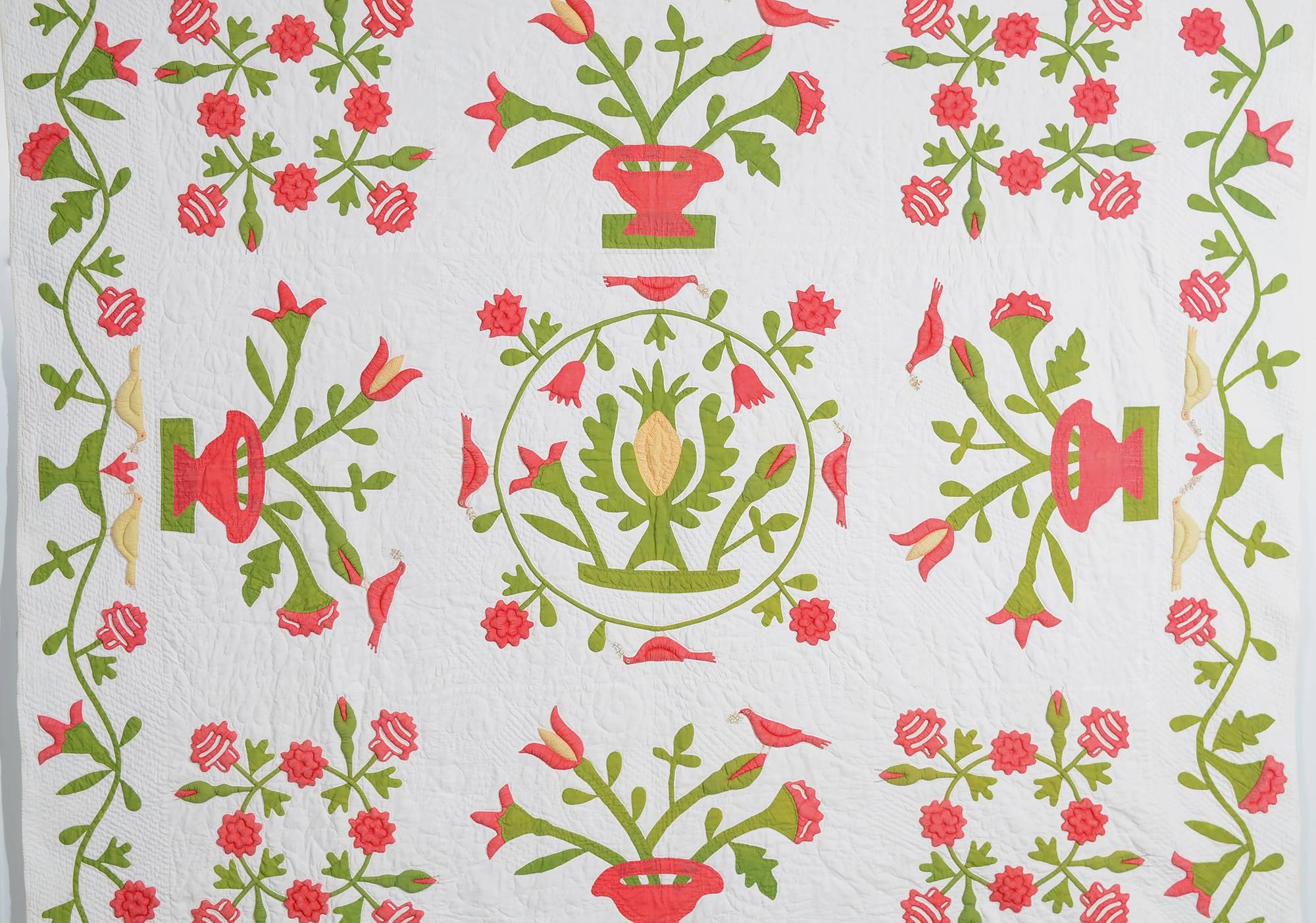 This folky center medallion quilt is a complete original. The pineapple in the center is the traditional symbol for hospitality. Surrounding it are symmetrically placed floral wreaths and baskets of flowers upon which sits a bird in each. The same