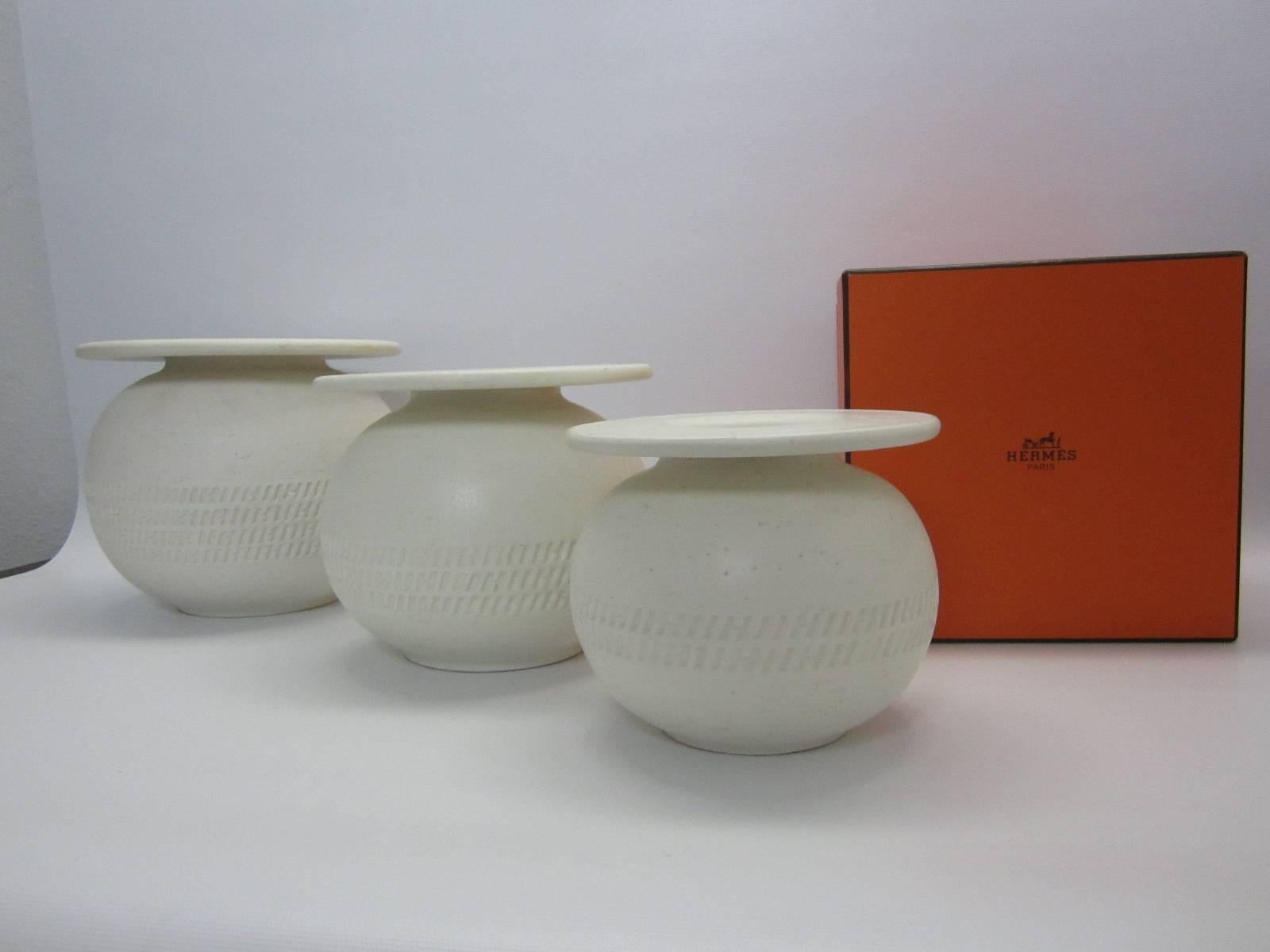 Group of three white textured clay pots in graduating size. Each pot has an  Hermes 