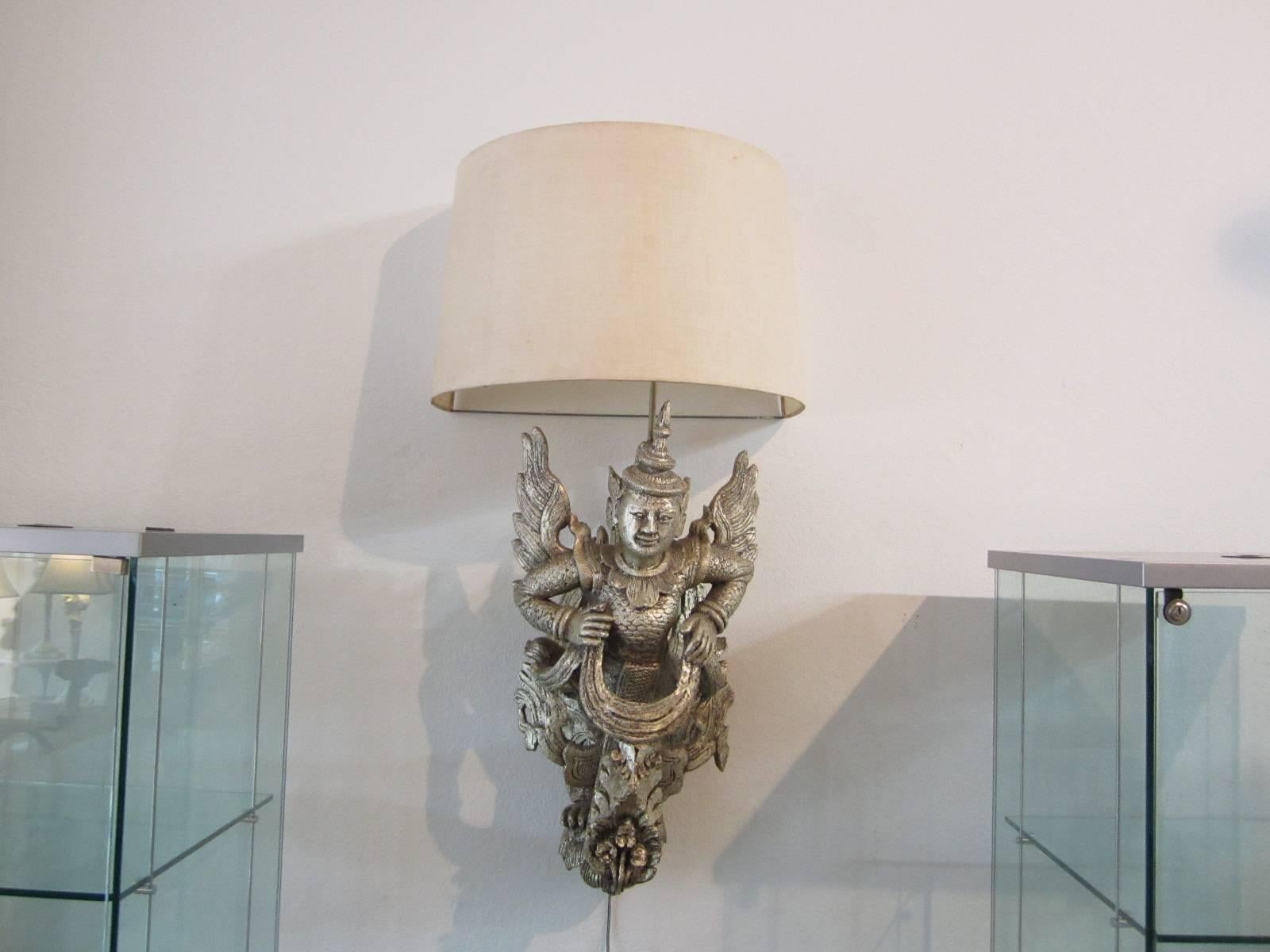 Winged wall sconce with intricate design painted in a rough silver finish creating the patinated silver leaf look. On/off switch on lower righthand side and comes with its original half moon shade as found in a Palm Springs, California James Mont