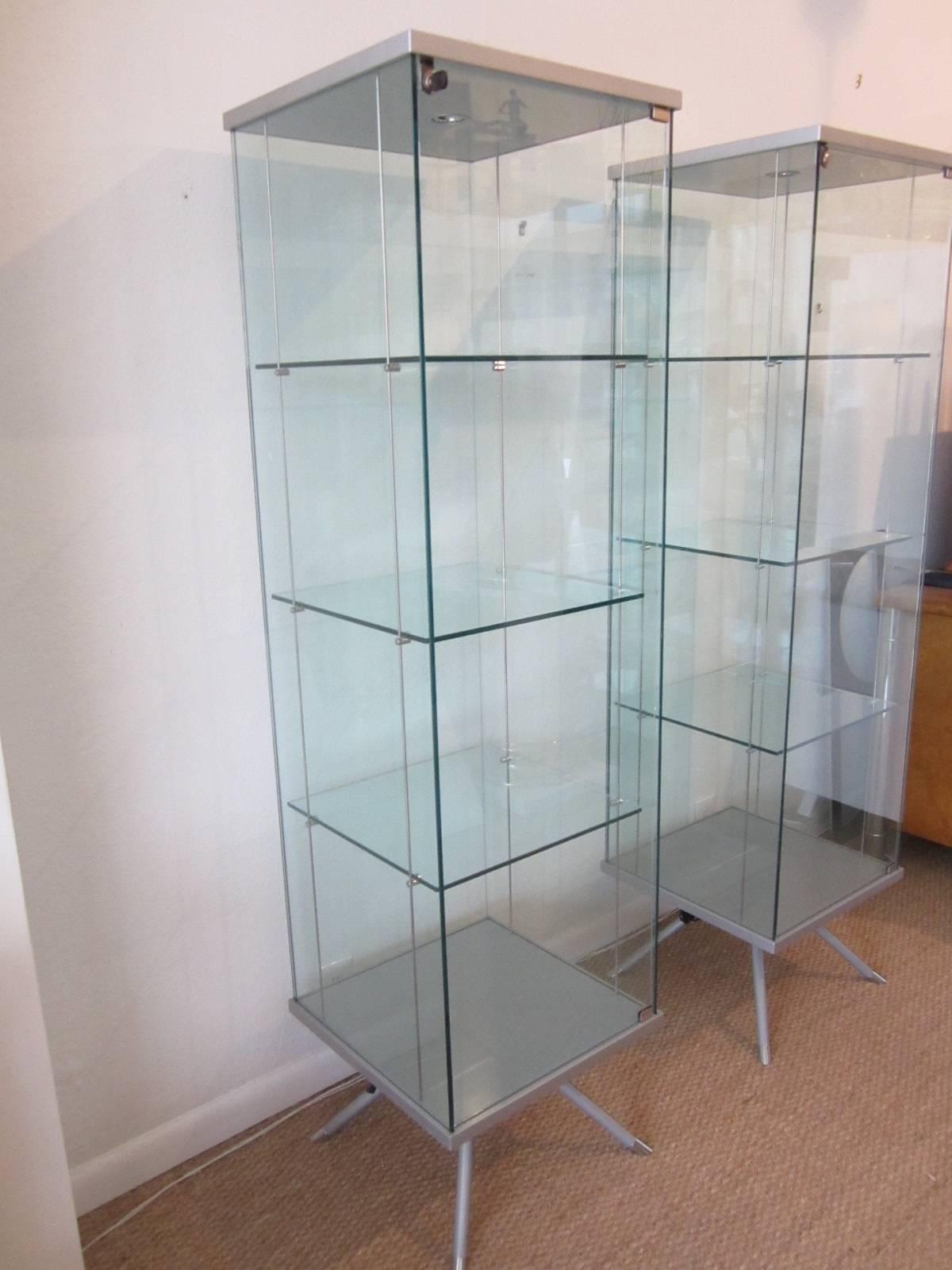 Italian vitrines in glass with matte metal framing and flared legs. Interior steel cable suspension holds pins for glass shelves to rest on. Upper interior light has original European wiring with attached US Standard plug. Each vitrine has lock and