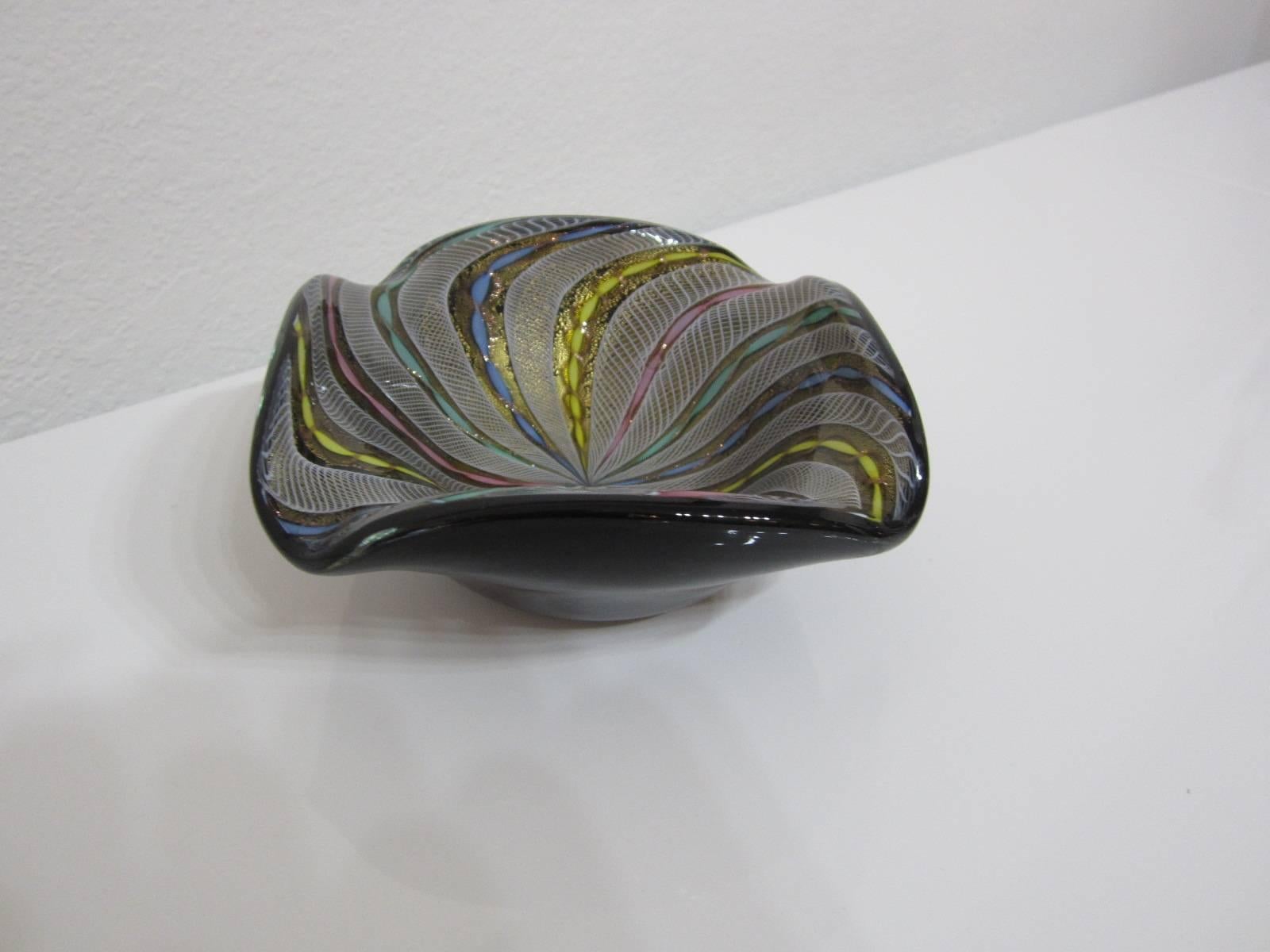 Handblown Murano glass bowl with beautiful, colorful latticino swirl interior pattern on black background glass.