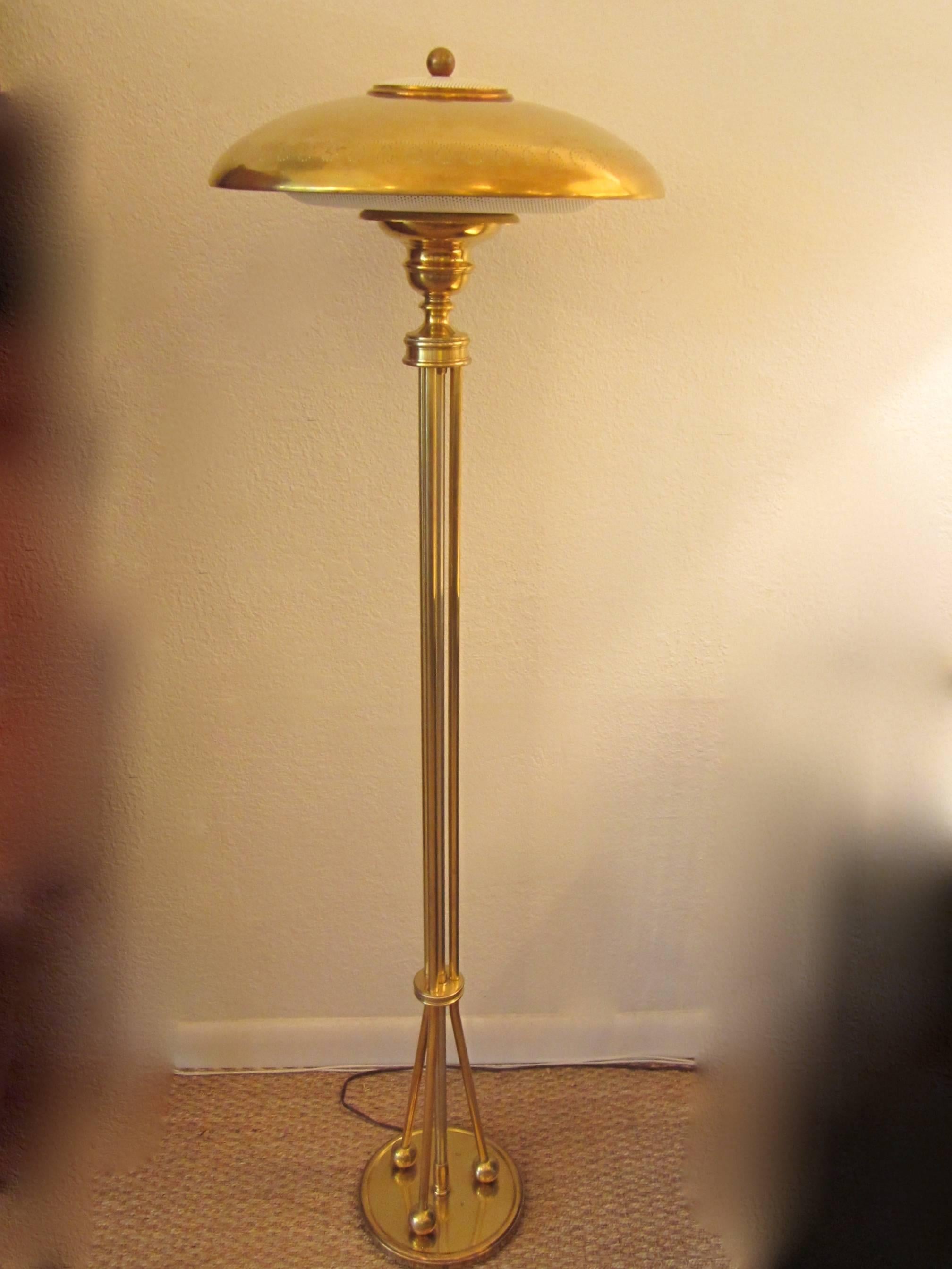 Beautiful solid brass standing floor lamp with perforated shade. White metal perforated diffusers on top and under shade. Three rods at end of center pole terminate with ball feet at the base. Original turn switch and finial.
The shade measures 16