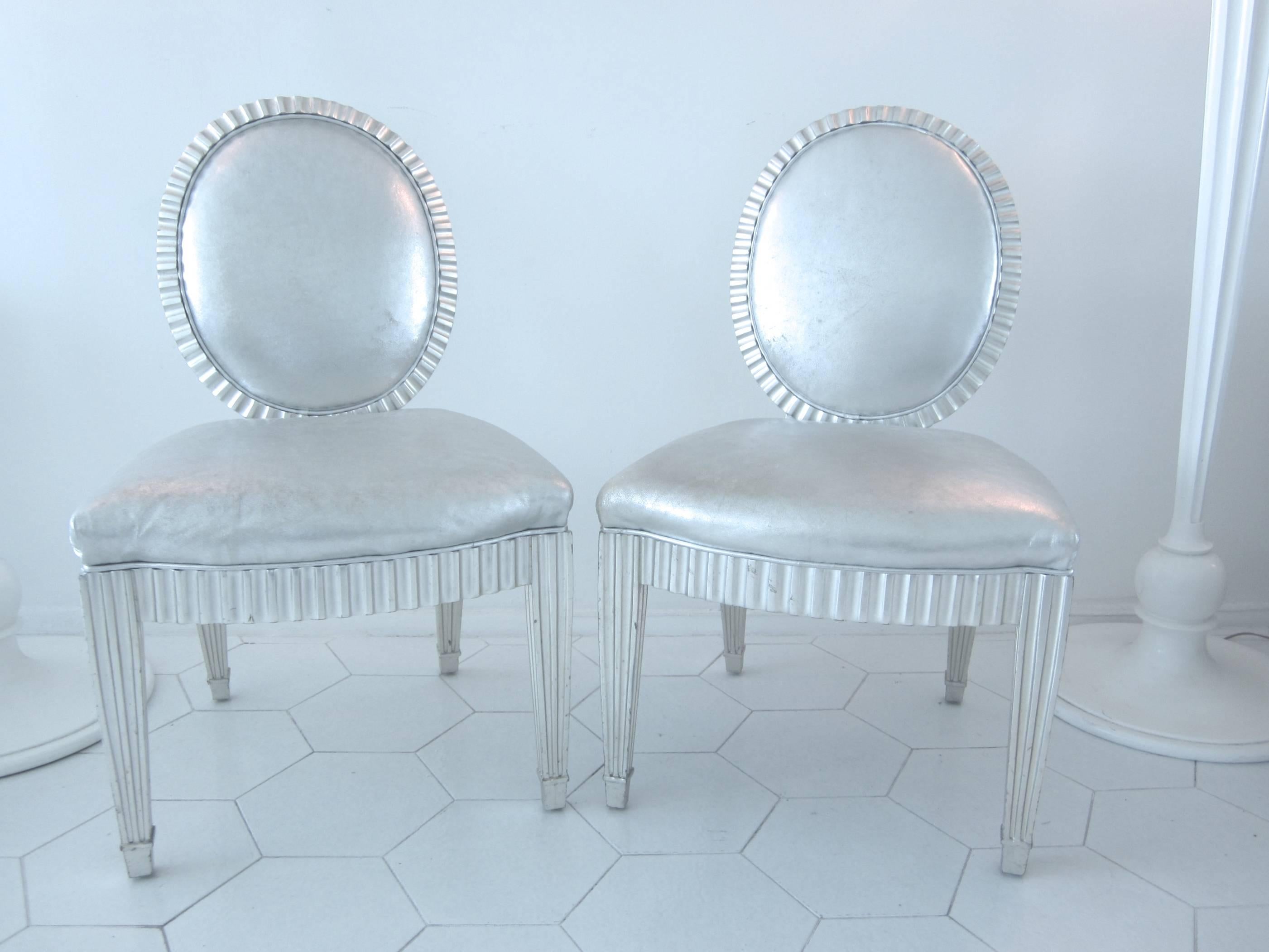 Gorgeous pair of neoclassical chairs with silver leaf wood frames and silver metallic leather cushions. Shows natural wear.