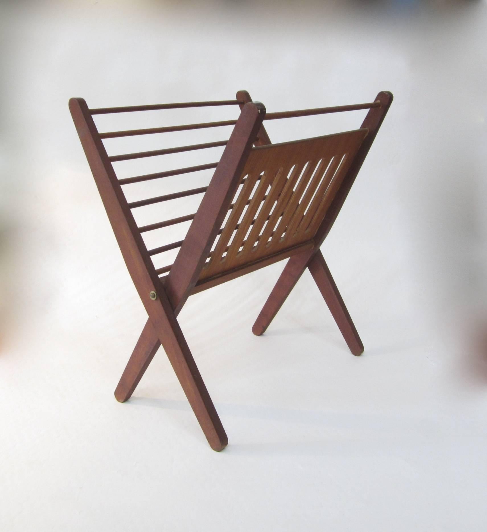 Folding teak magazine holder featuring vertical slats on one side and horizontal rods on the other. Sturdy and solid.