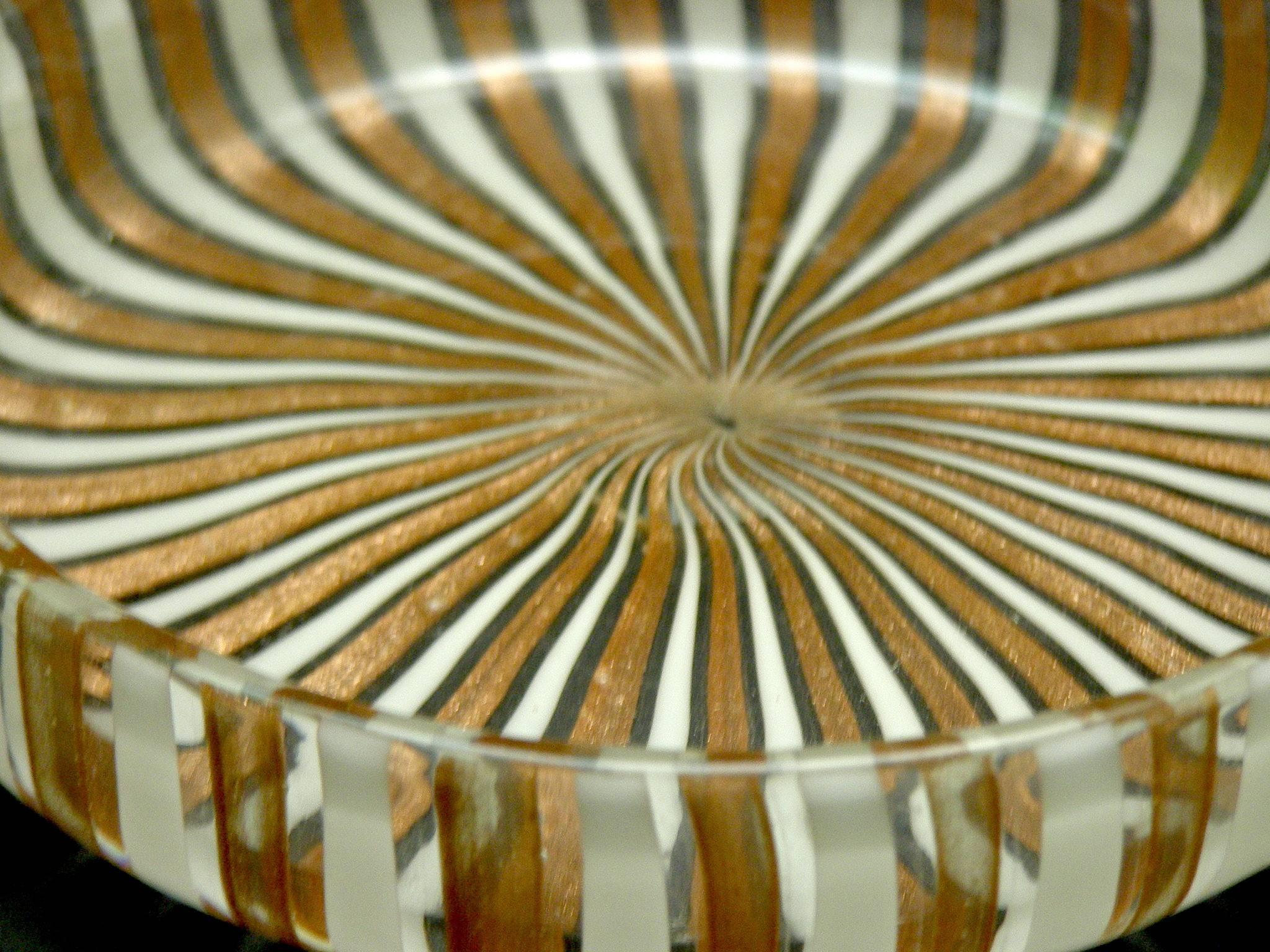 Beautiful handblown Murano glass circular dish with raised rim. The caning technique was used to create the stripes that are in copper and white and give this dish a wonder presence. Although this dish or bowl is not very large, it has weight to it