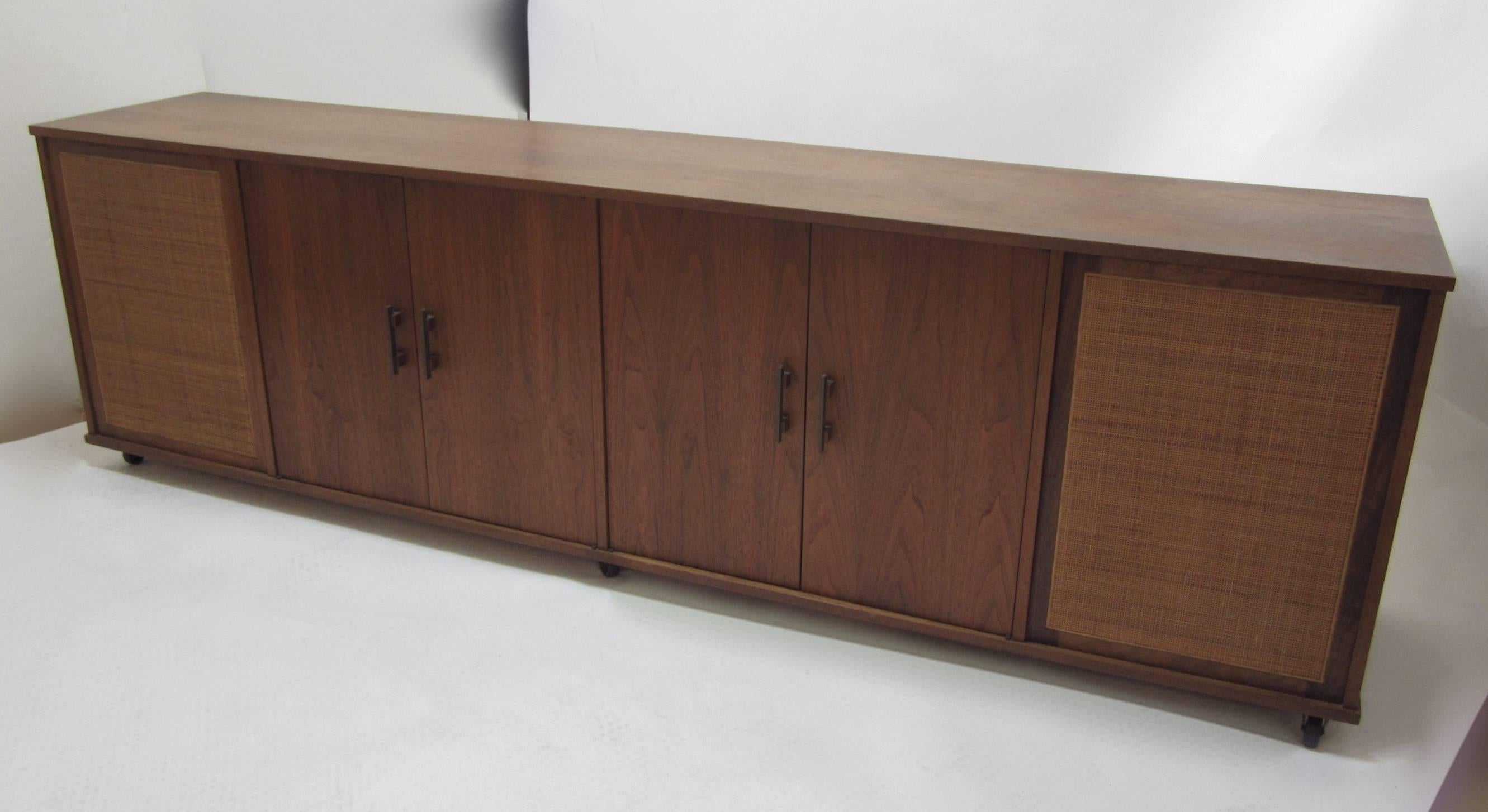 Fantastic eight foot long media cabinet designed to hold records and stereo equipment and speakers behind the caned-front compartments. The interior has been redesigned and the speakers and some shelving have been removed in an amateur fashion but