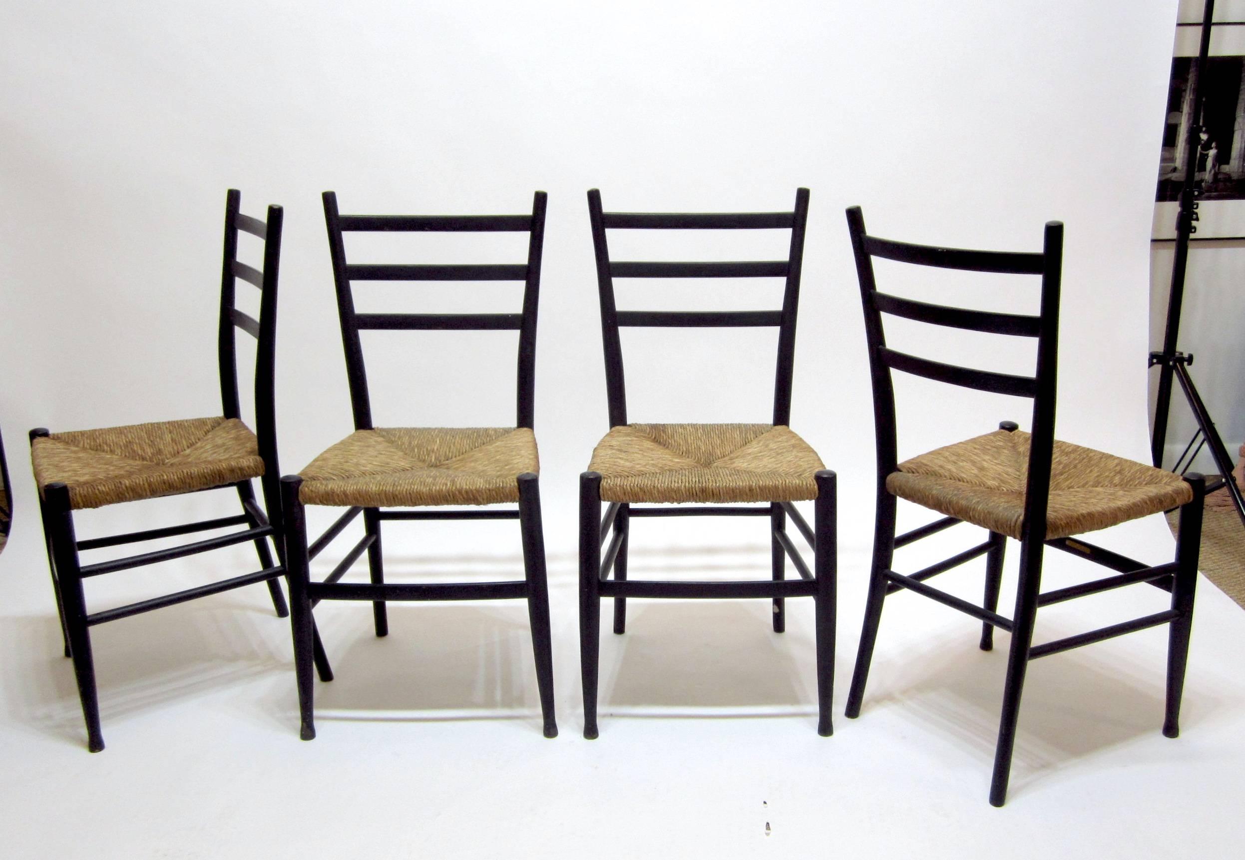 Set of four black painted wood ladder back chairs with rush seats. The seats are in excellent condition and the painted wood frames show normal wear, no breaks or damage.