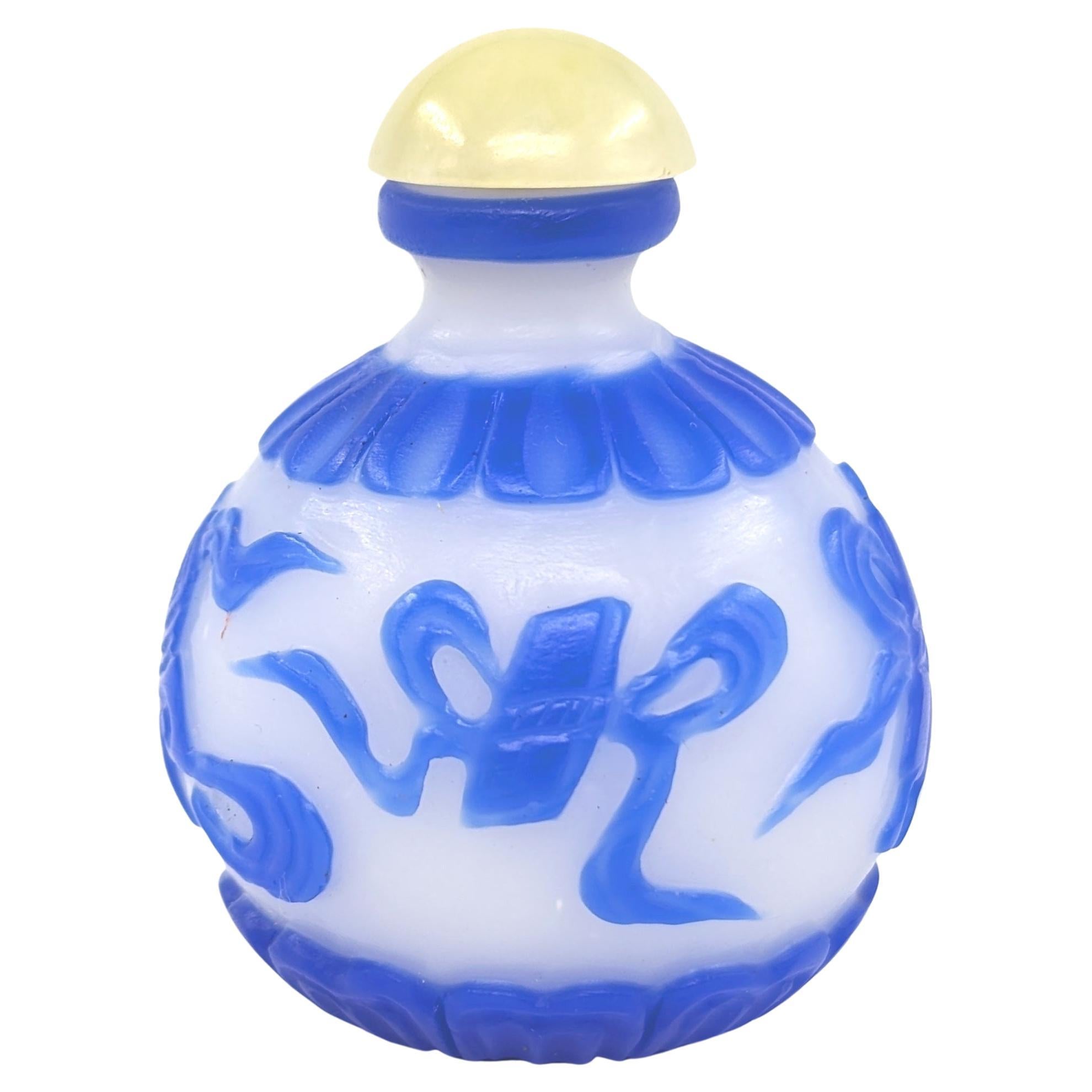 A Chinese blue color Peking glass overlay snuff bottle in globular form, on pale white ground, hand carved and decorated with four Buddhist treasures , on a slightly raised footring, and with a jade cabochon stopper

weight: 43 Grams
circa: Late