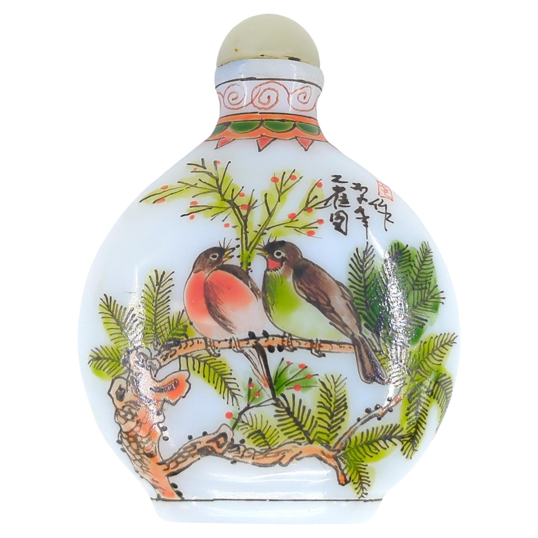 This Chinese snuff bottle is a delicate and vibrant piece, crafted from milk glass and adorned with enamel painting. The bottle features a cabochon jade stopper, adding a touch of elegance and luxury to the piece.

On each side of the bottle, there