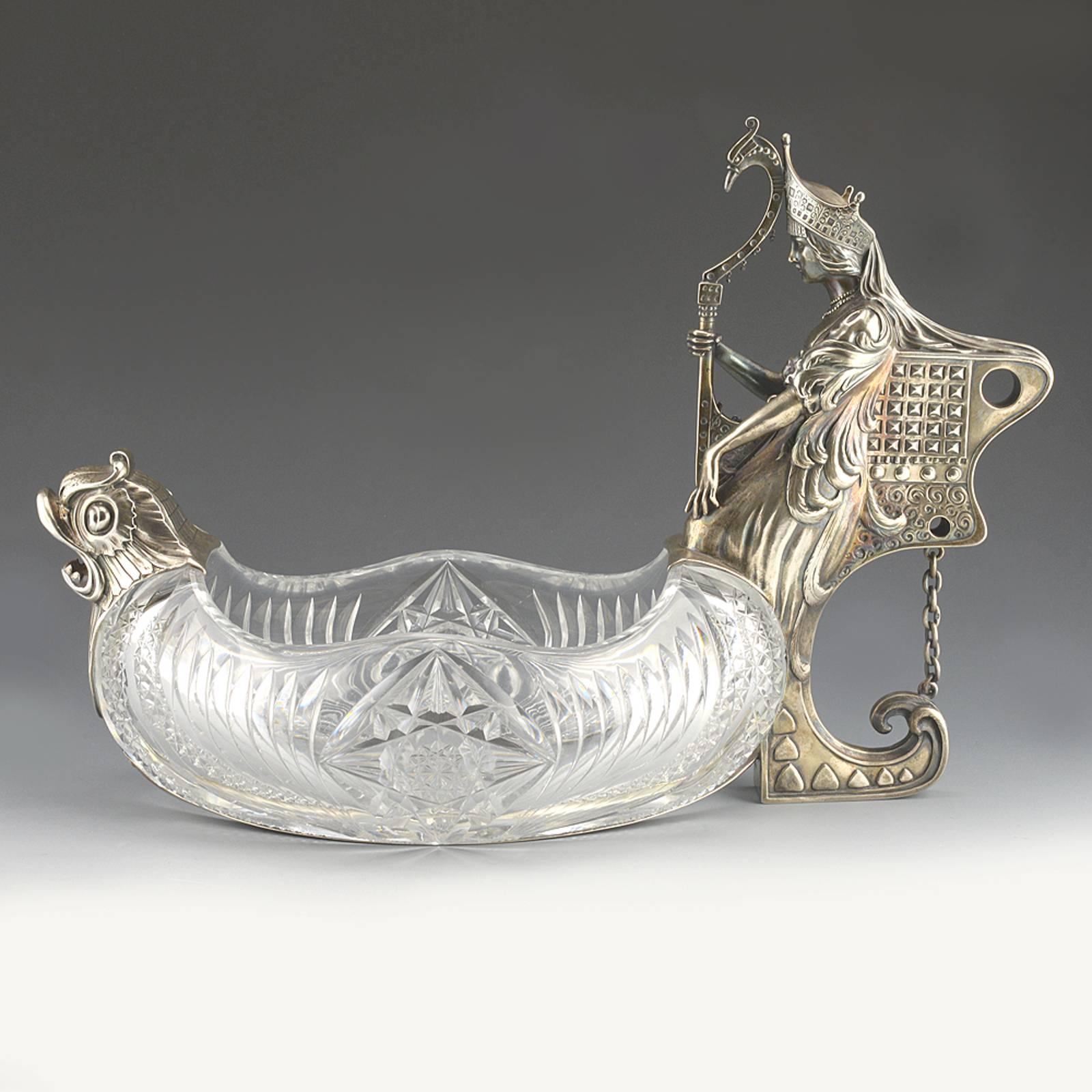 A large silver-mounted cut-glass kovsh form centerpiece, Khlebnikov, Moscow, 1908-1917. The handle cast and chased as a Swan Maiden in the clothing of a Boyarina in Kokoshnik, holding her swan-headed harp in one hand and with feathers from her