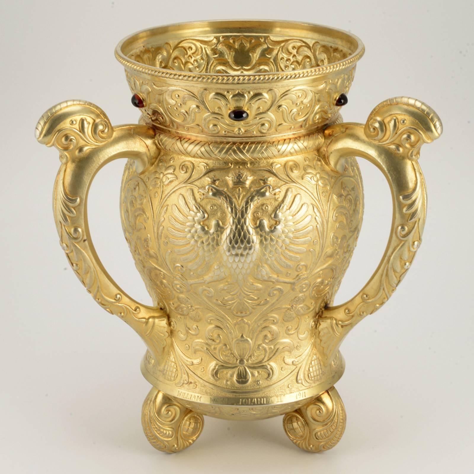 A Russian gem-set gilded silver three-handled loving cup yachting trophy, Ovchinnikov, Moscow, 1908-1911. The body of baluster form with flaring neck, chased and repoussé with three double-headed Imperial eagles within chased Usolk-style floral and