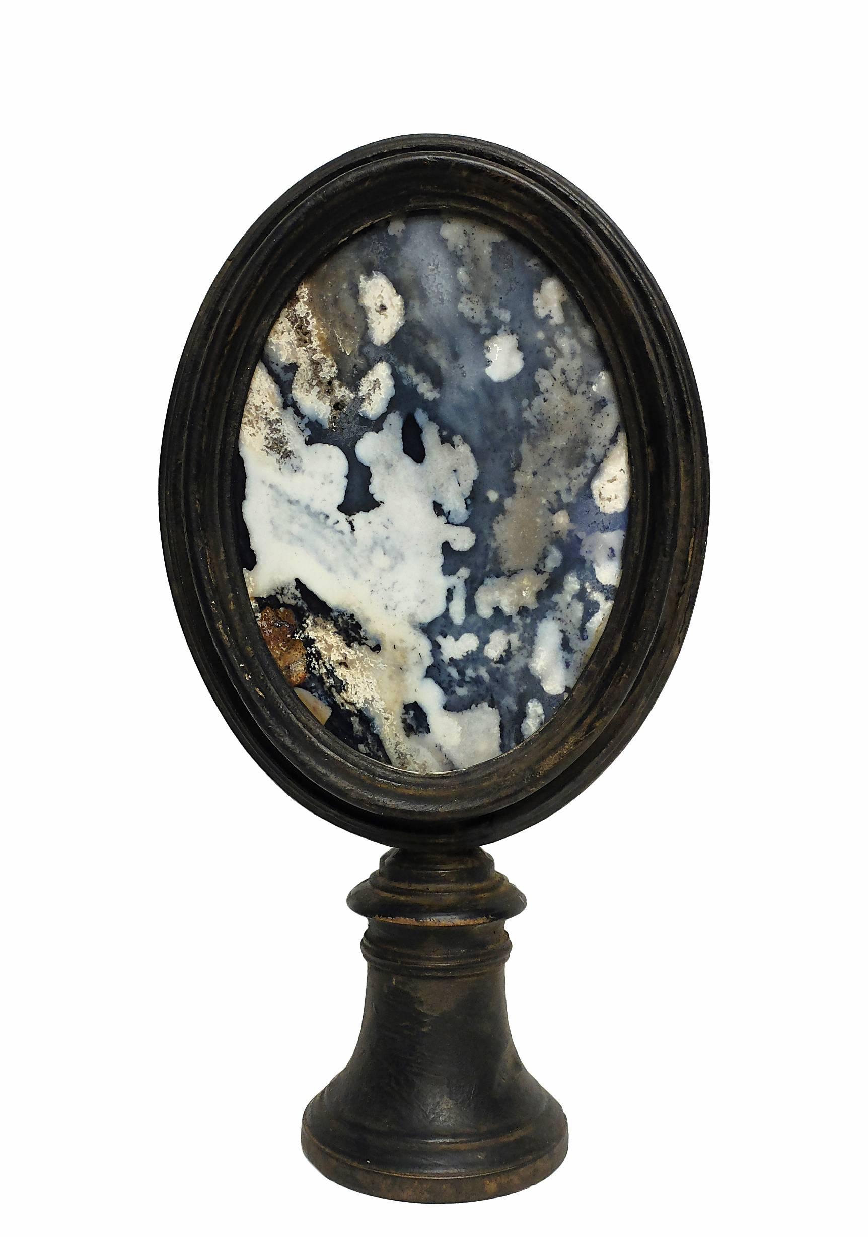 A couple of Wunderkammer naturalia oval shape spotted blu - gray agate marbled specimens with black wooden frames, mounted over black wooden bases, with candle holders, Italy, circa 1880.
    