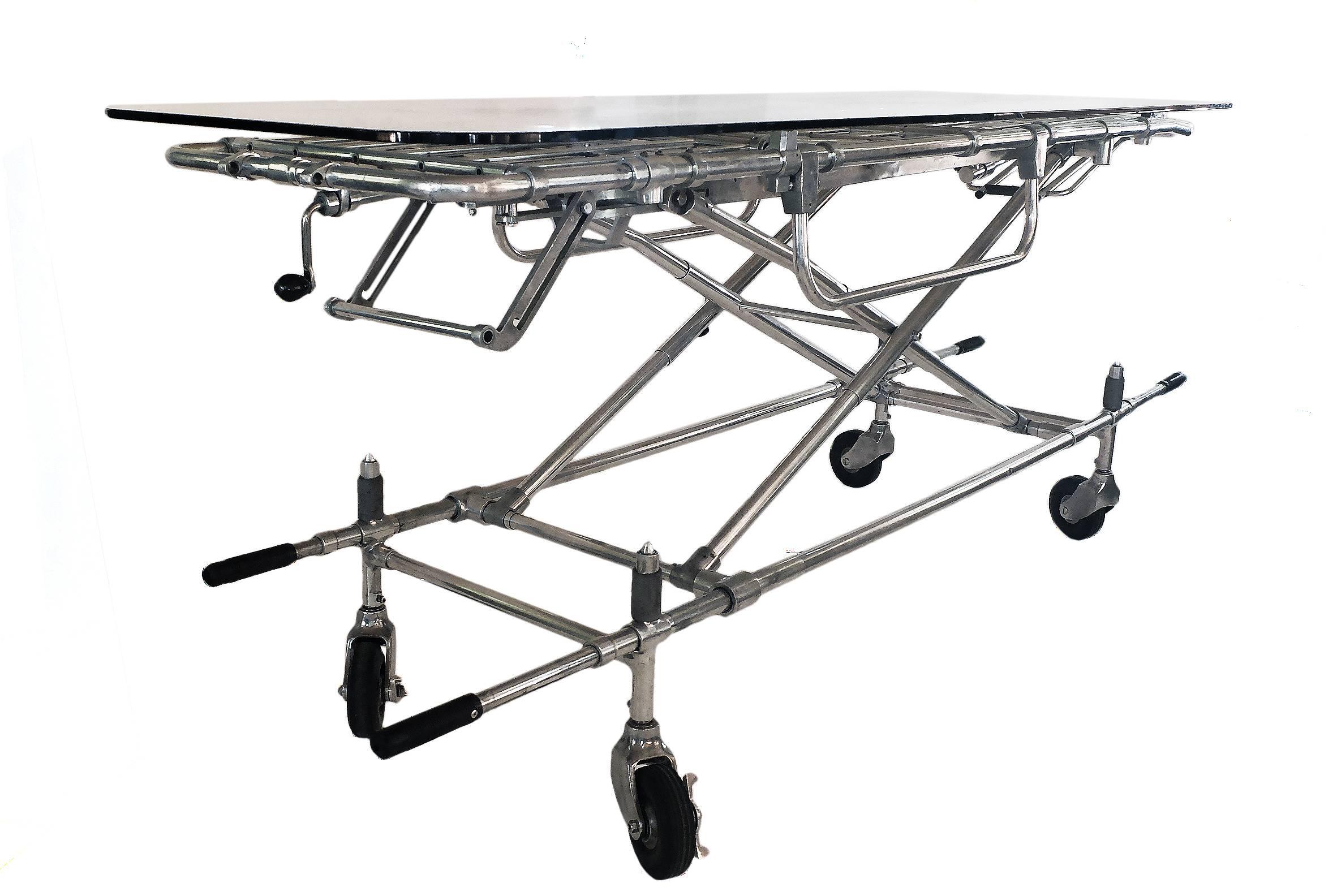 A fine example of reinterpretation and realization of an old element. A chrome metal gurney from ambulance with wheels has been reused as a basis of an adjustable dining or coffee table, from 16 inches to 40 inches. The tabletop is made out of a