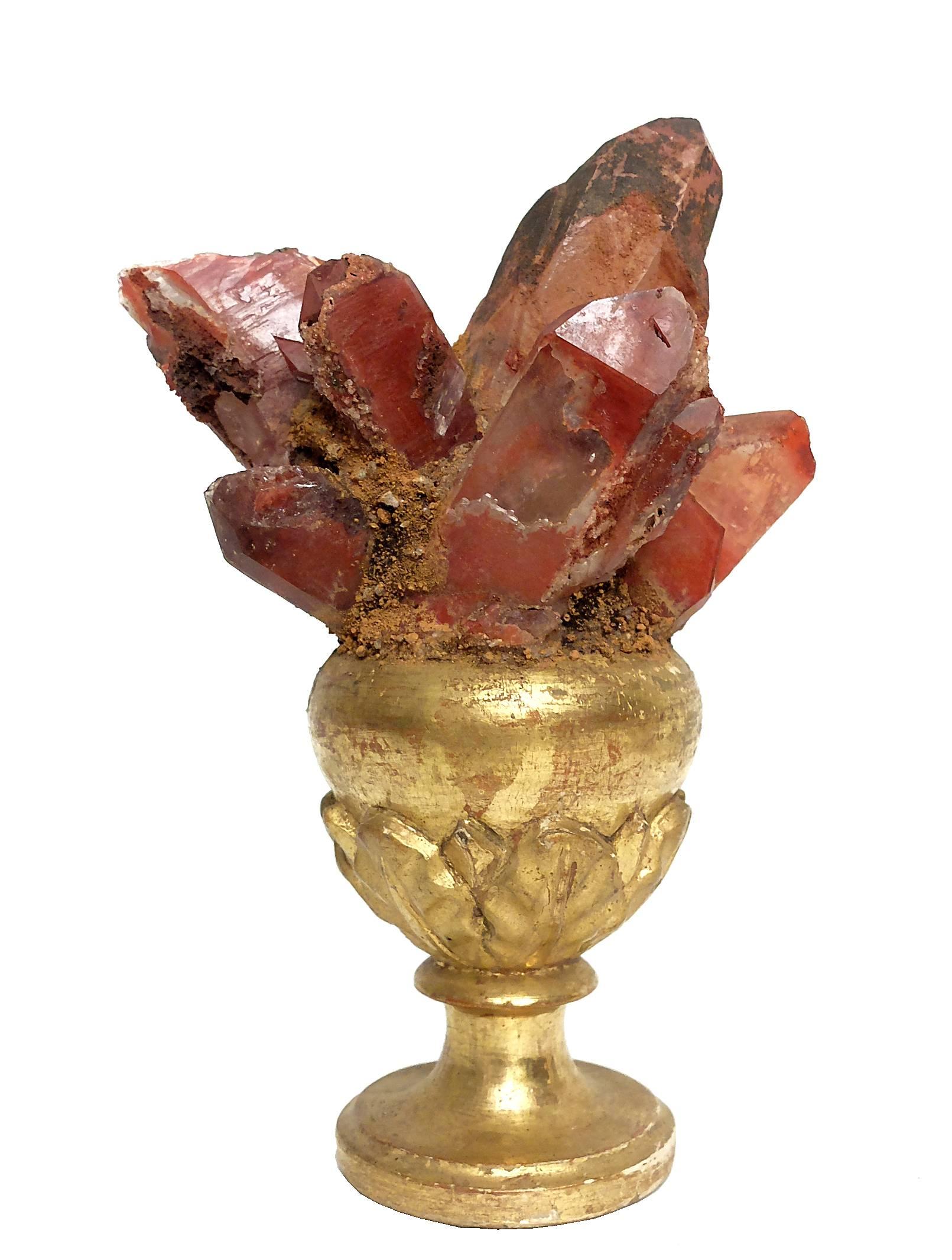 A Naturalia mineral specimen a pair of red crystals, mounted over older guild-plated wooden bases on a vase shape with leaves.