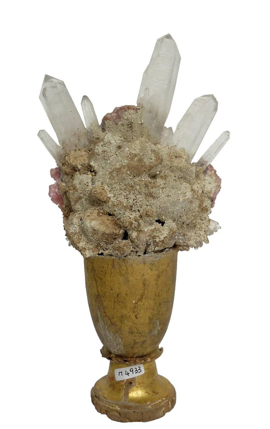 A naturalia mineral specimen a druze of rock crystal quartz and pink quartz. It shows a wooden base, finished with pastiglia, and gold leaves. The quartz sample are mounted over the base .