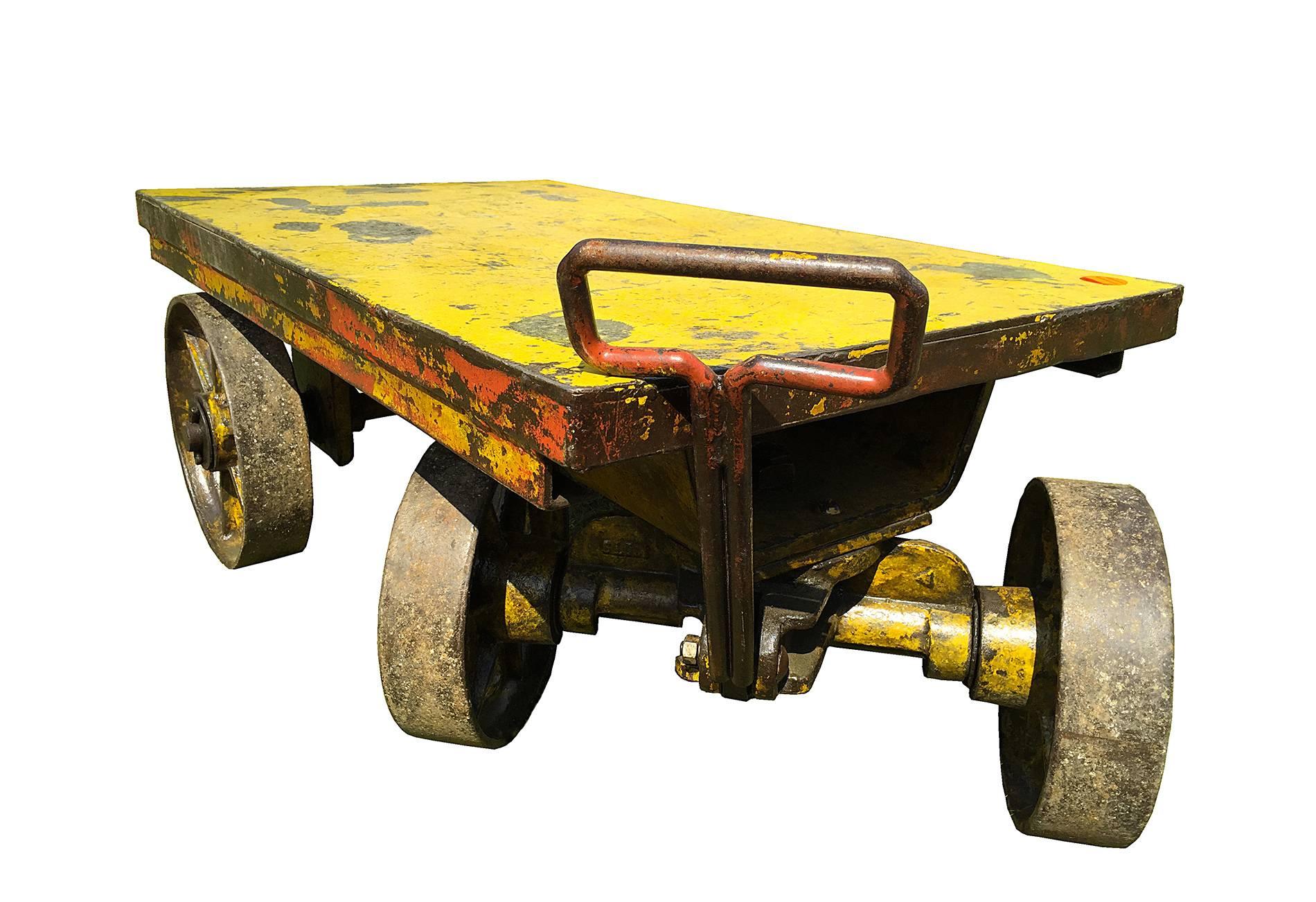 Iron and cast iron industrial wheelbarrow , rectangular shape , with 4 big wheels (11” diameter) and a long handle that allowing the front wheels to rotate . The top shelf has a thickness of 4 “ .
