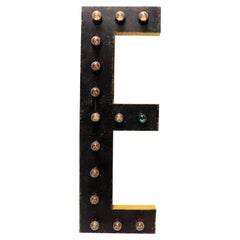 Large black and yellow tin letter E illuminated by light bulbs. USA 1930.