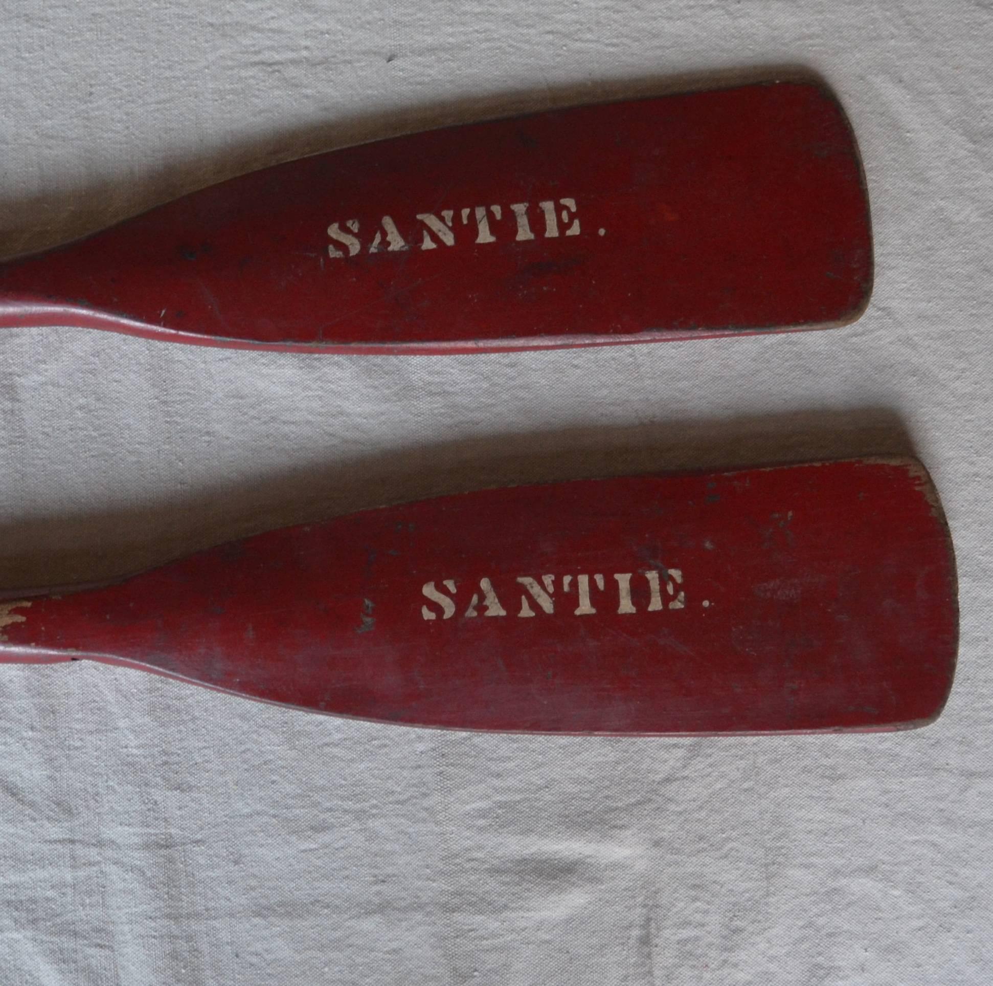 Old painted short canoe oars with nice red paint with white lettering. Hand-wrought iron grips add to their texture and appeal.