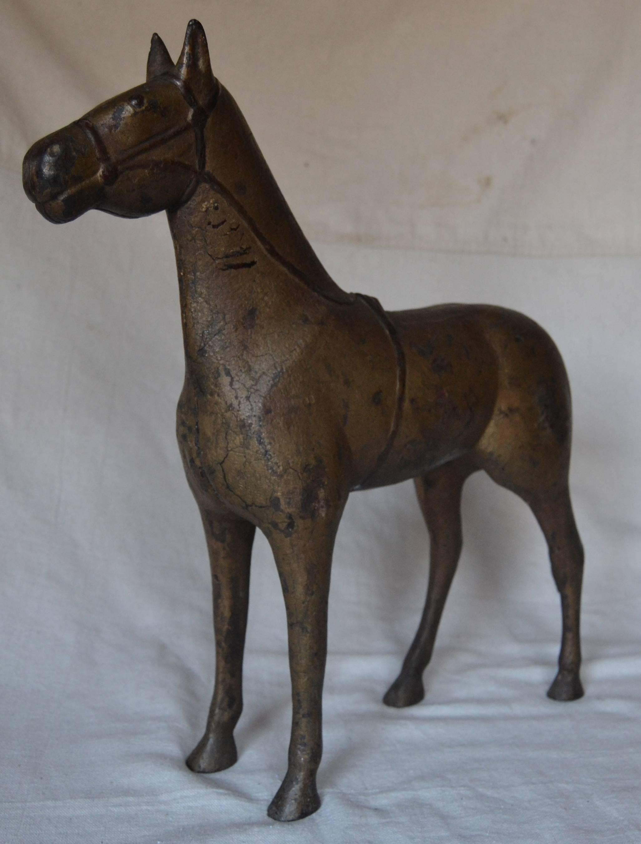 Very good folky cast iron rendition of a standing horse with great details. Whimsically detailed form of the tail with the sharp line of the bridle providing additional visual interest. Old painted surface of tarnished gold with reddish color to the
