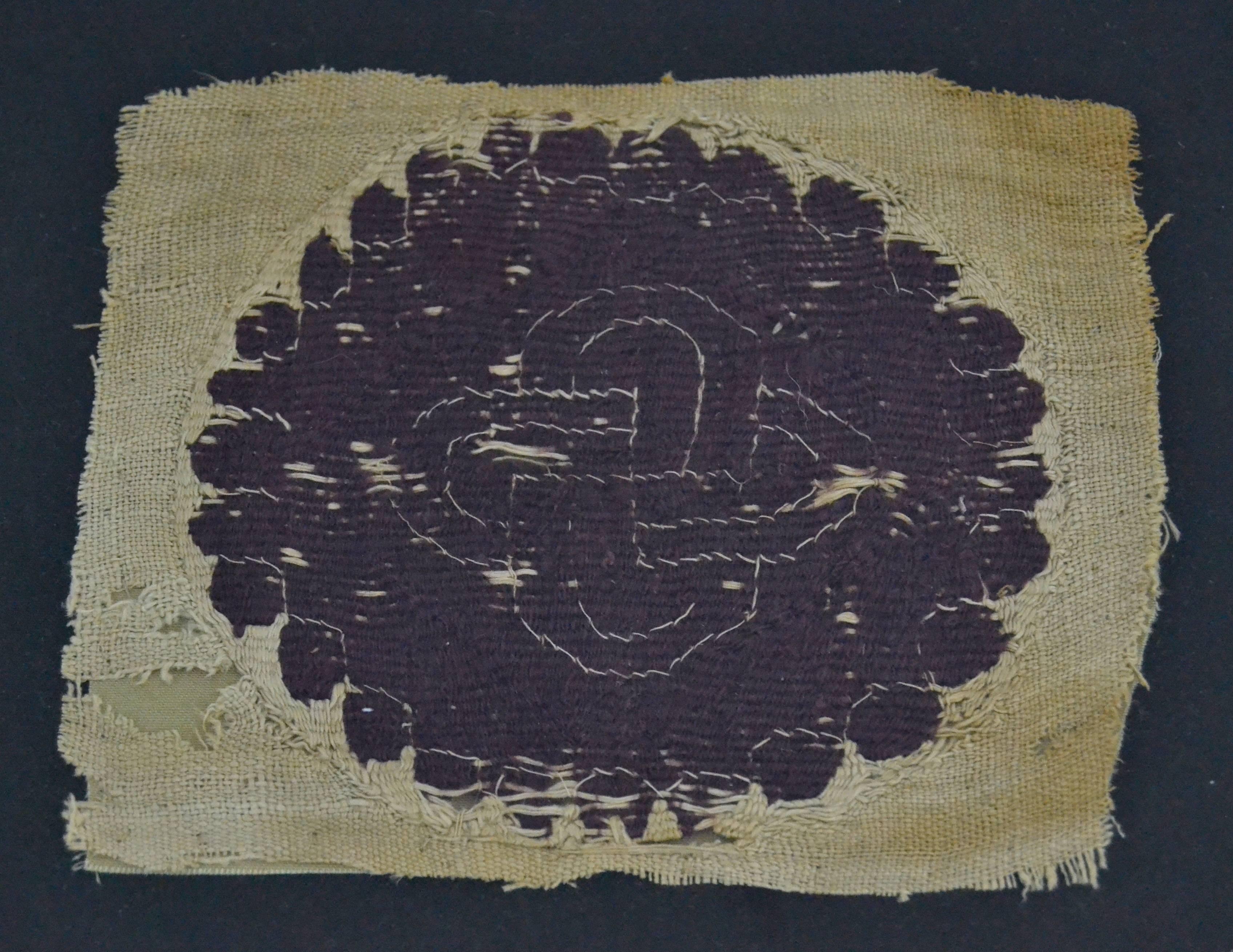 Coptic roundel of a Herakles knot, plain woven linen with tapestry inserts. the fragment is mounted on linen and in a plexiglass box.