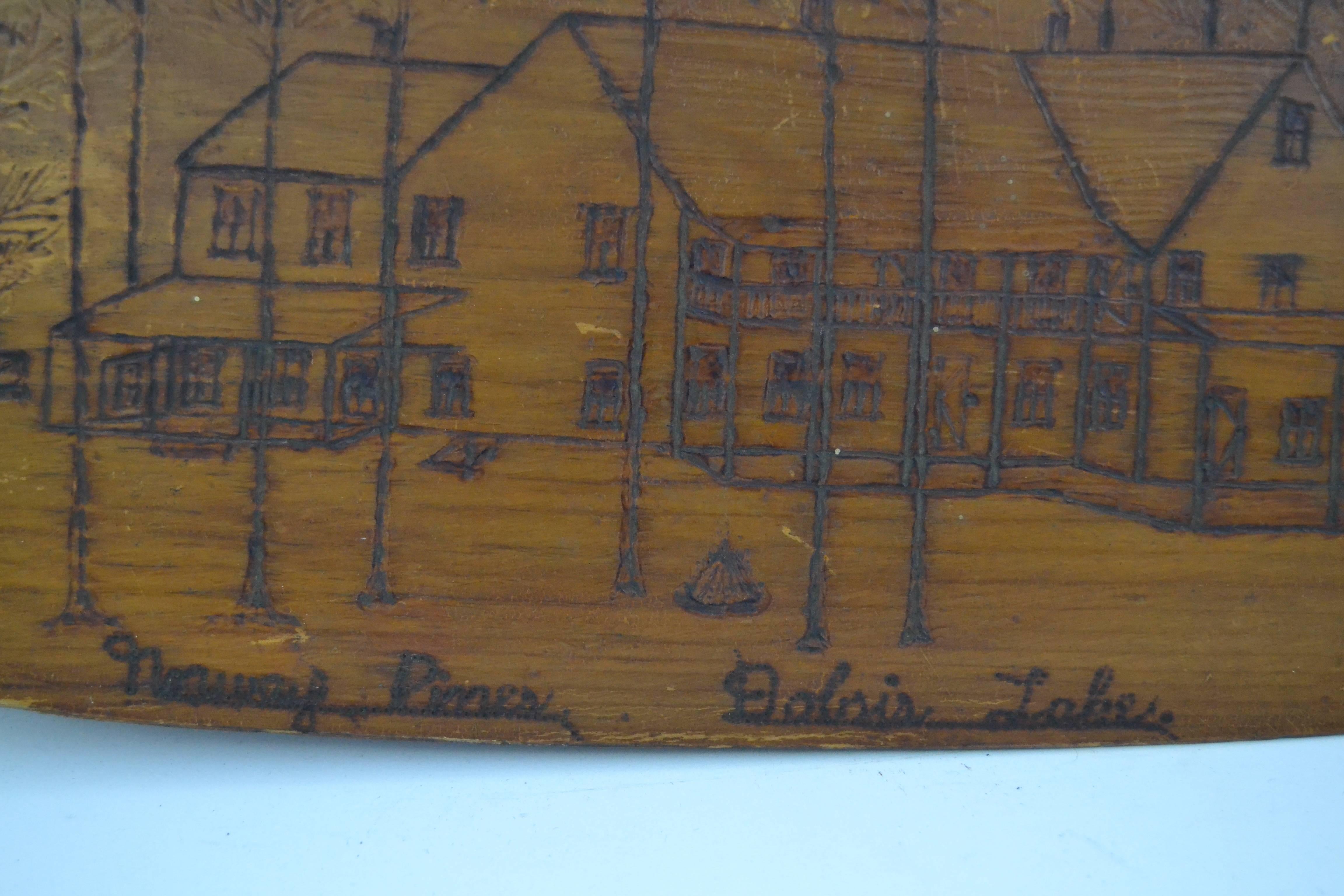 Carved pine canoe paddle with exceptional folk scene of the "Norway Pines at  Dobsis Lake". The pyrography image depicts the main lodge which was built in 1884 on lake Syladobsis in Orrington Maine. Notable visitors to the lodge included