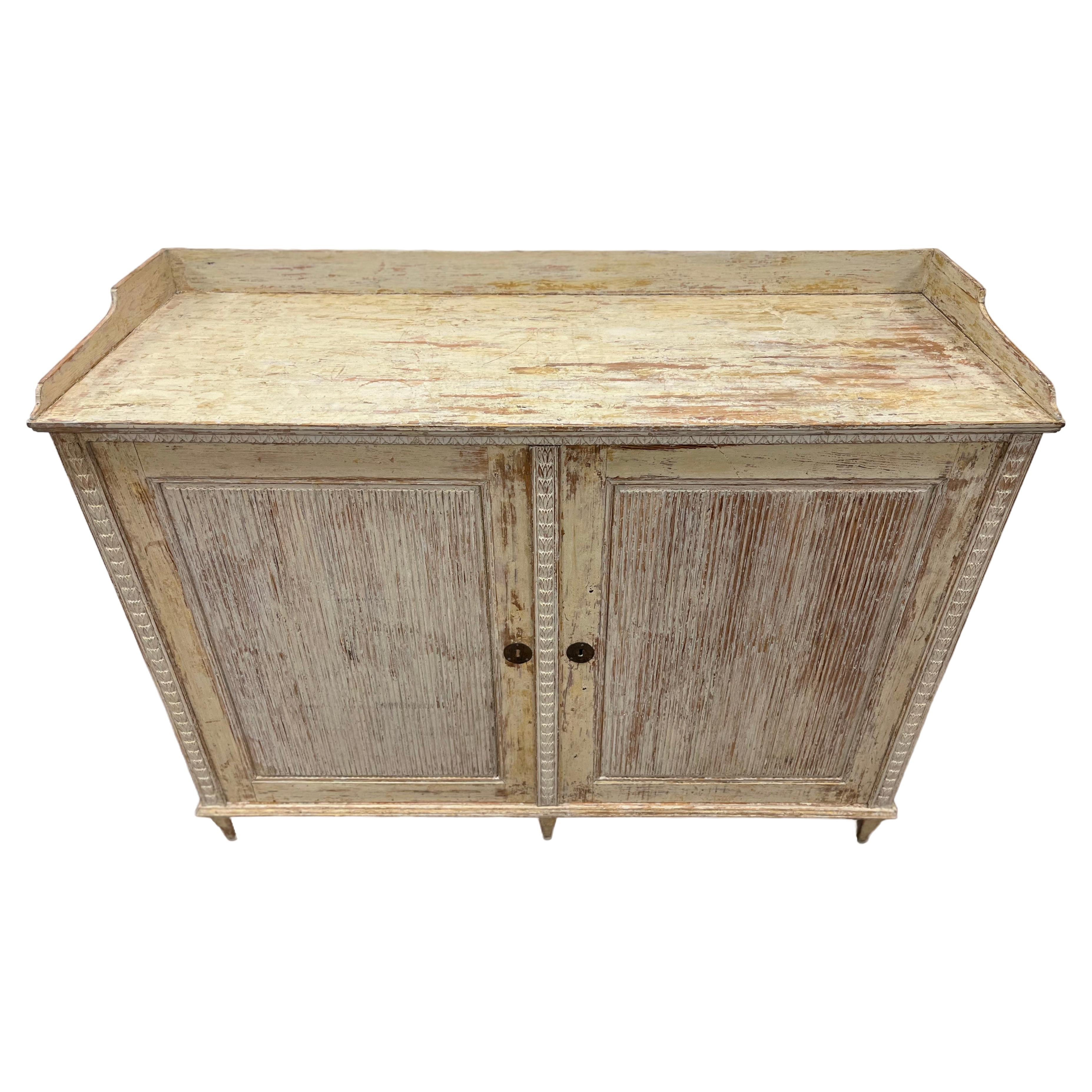 A beautiful Swedish Gustavian sideboard made in Angermanland with elaborate wood carvings – reeded door fronts, leaf cut detail at the top and wheat sheath décor on the sides. Interior has three shelves. Neatly scraped to its original cream colored