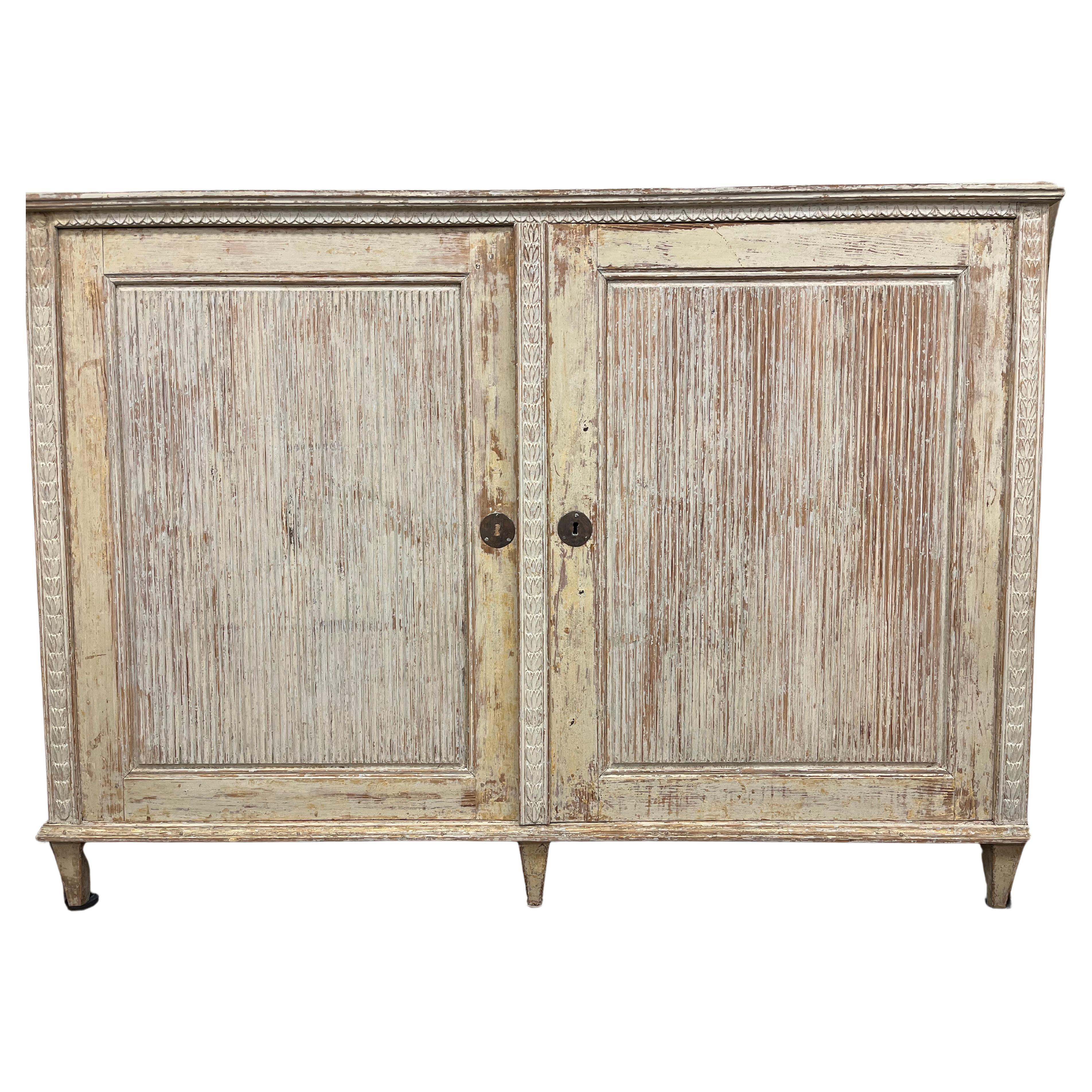 A beautiful Swedish Gustavian sideboard made in Angermanland with elaborate wood carvings – reeded door fronts, leaf cut detail at the top and wheat sheath décor on the sides. Interior has three shelves. Neatly scraped to its original cream colored