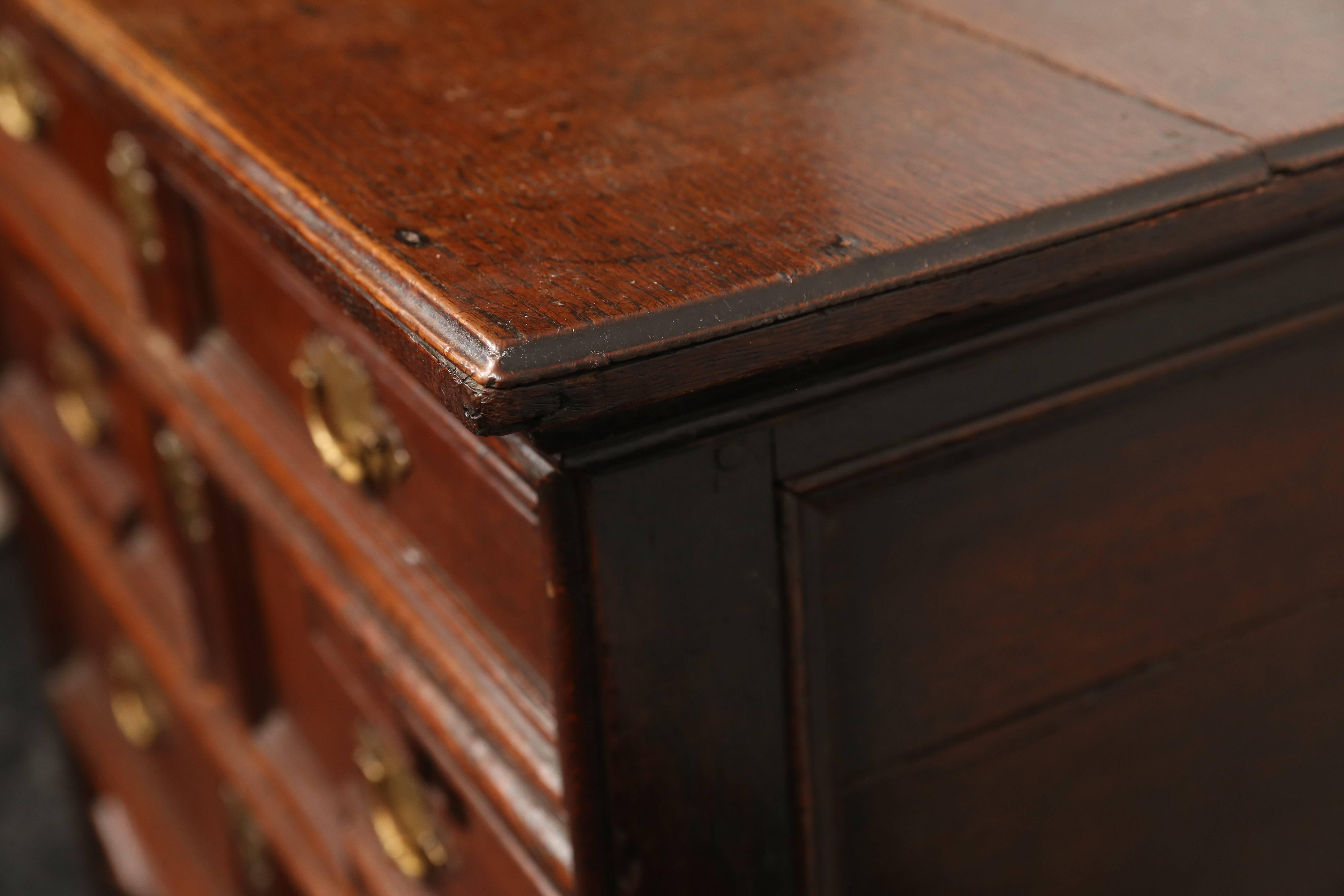 An early 18th century oak chest of drawers. The edge moulded top above four long graduated drawers with decorative geometric moldings, fitted with brass swing handles on shaped back plates embellished with engraving and punch work. Standing on