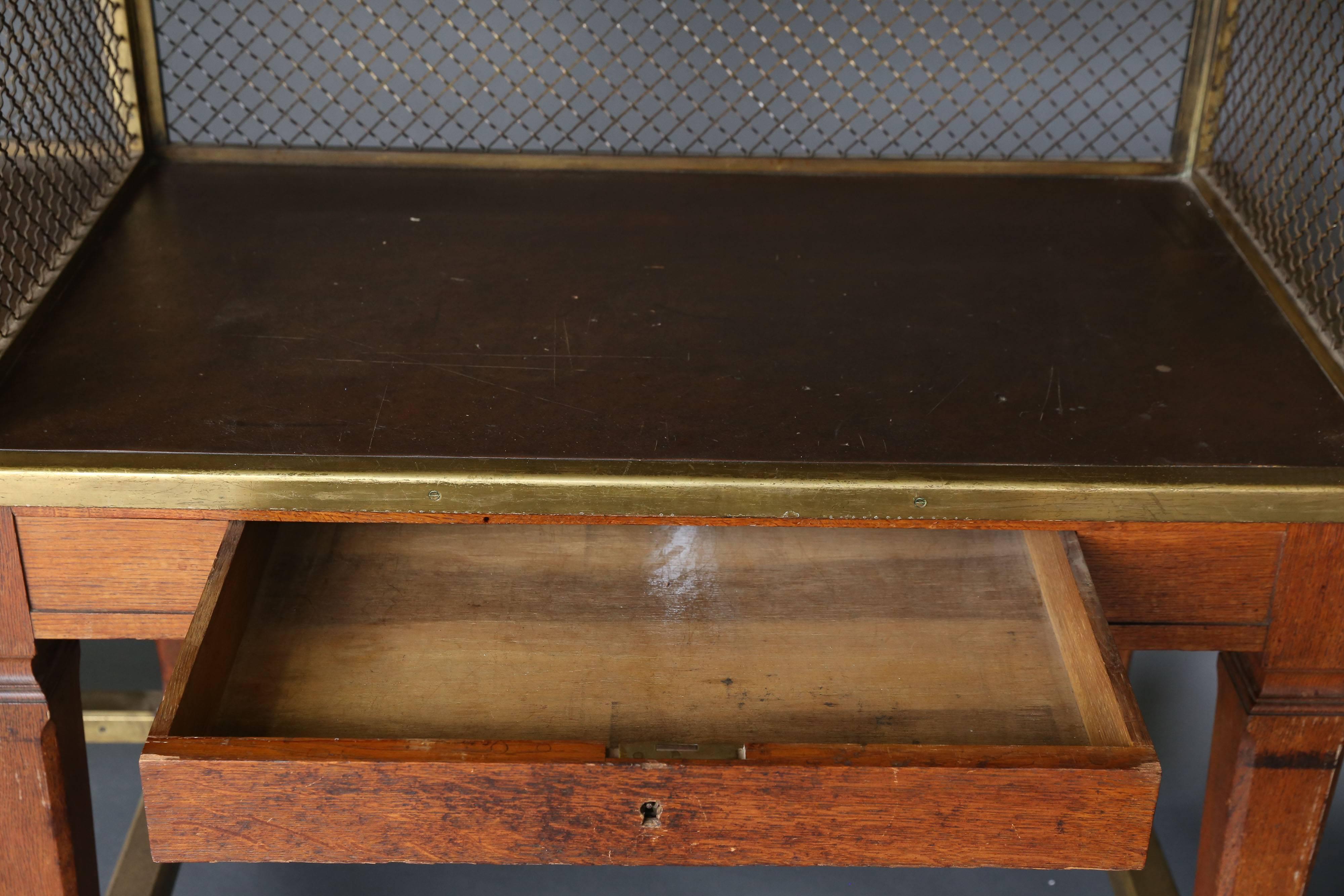 19th century oak and brass bank work counter that would work as a double desk or make a great bar. There are two shelves on the back. Brass webbing on back, perimeter and sides. Measures: L 85" x W 25.5" x H 30" 47" to top shelf.