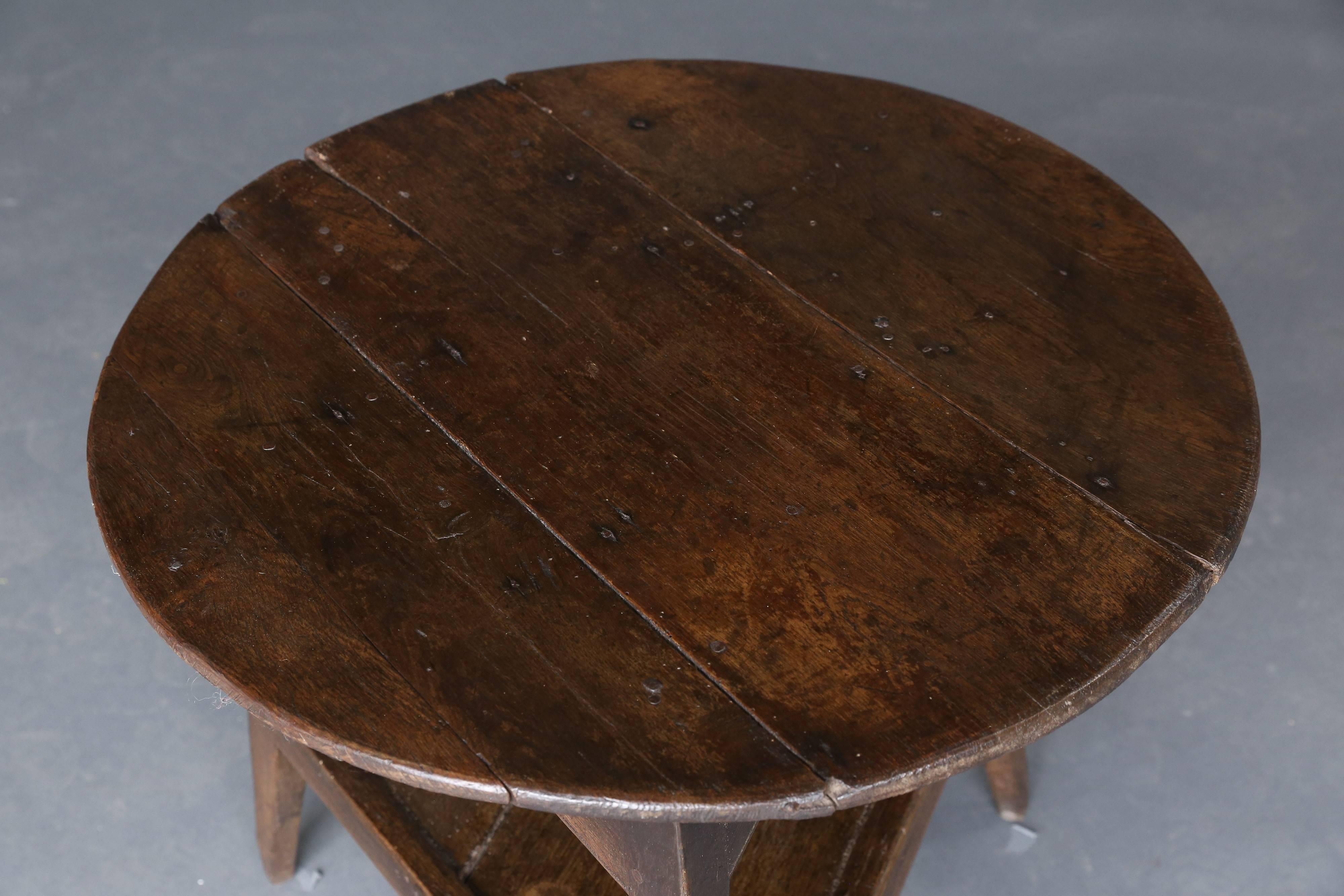 19th century oak cricket table with metal hand-wrought nails throughout top. Shelf underneath.