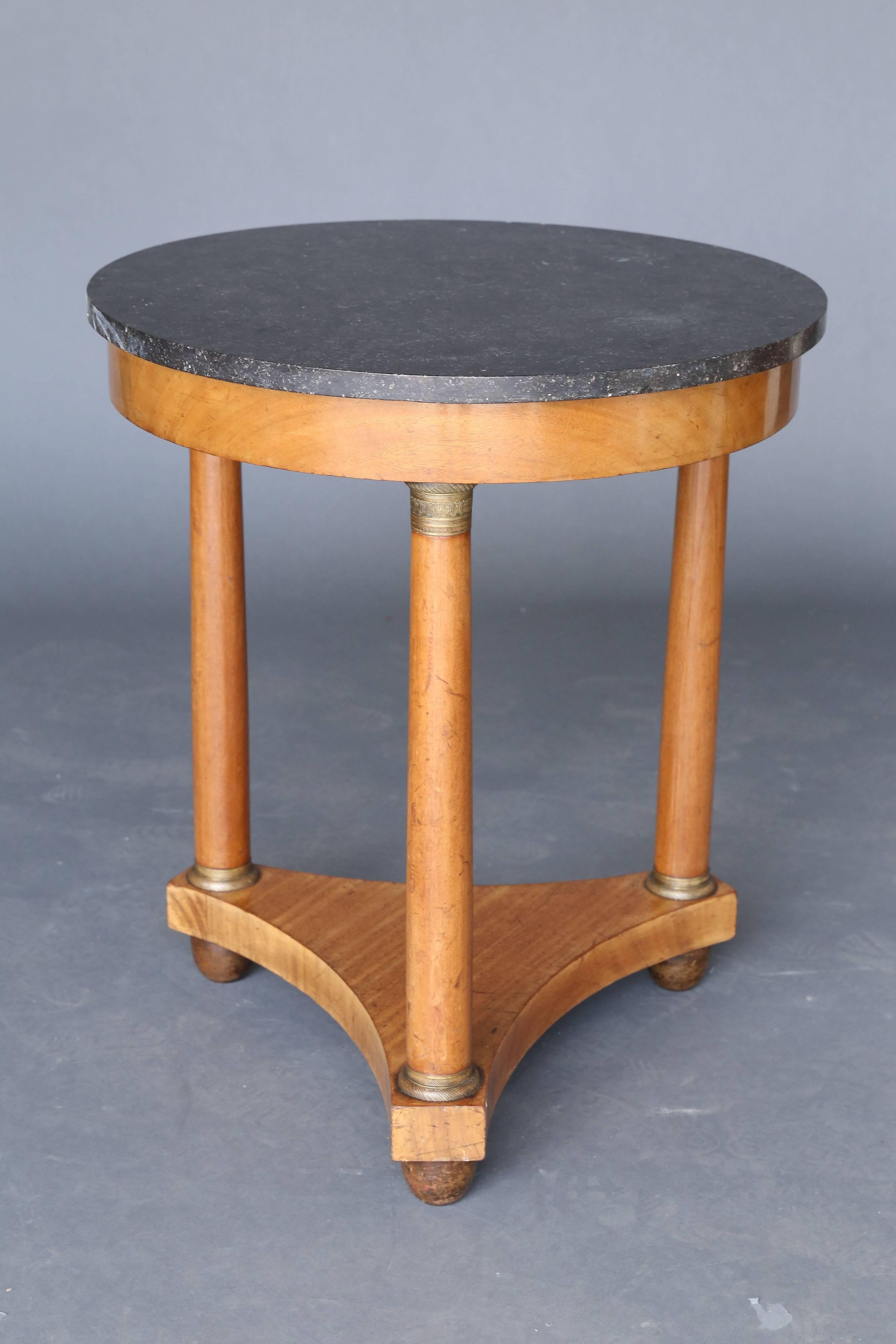 19th century Empire style marble table with a walnut base on three legs with metal detail. The legs rest on a thick wooden platform that in turn rests on three rounded feet under each of the columns.