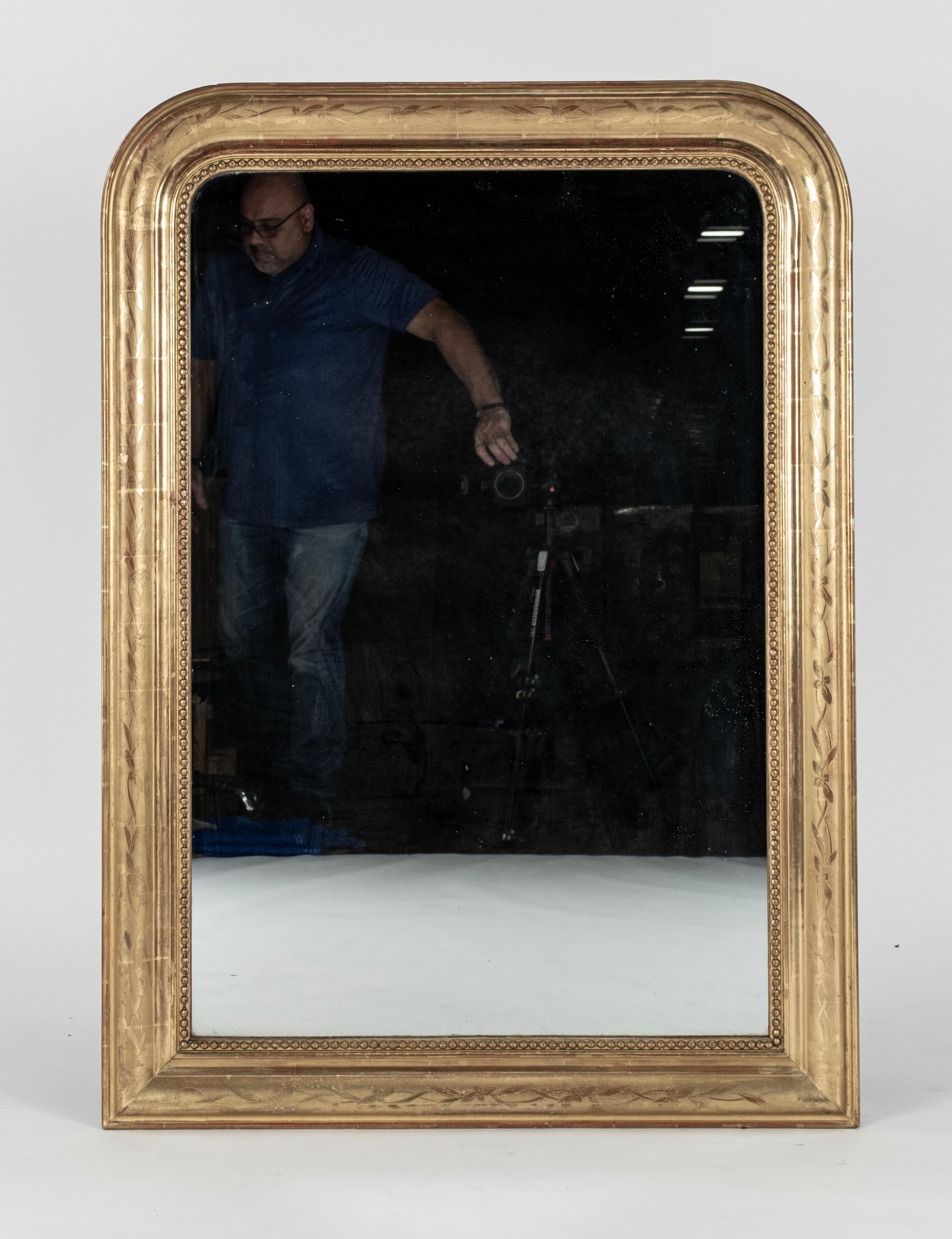  A fine example of a 19th century French Louis Philippe wall mirror. The wide wooden frame is in superb original condition with a decorative design of flowers and leaves etched into the gilded surface. A continuous row of plump gilded beads, called