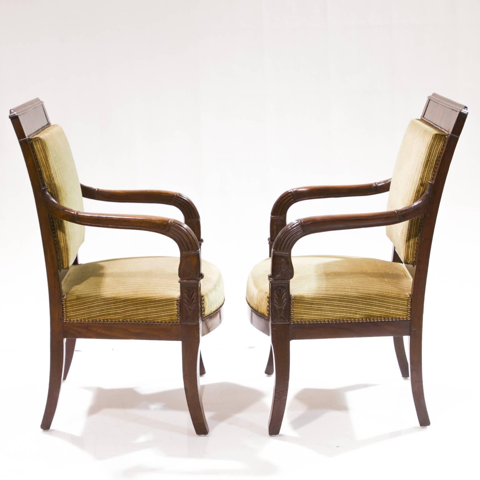A magnificent pair of French Empire mahogany open-arm chairs from the early 19th century. A fine French polish adorns the wood and give rich depth to the look of the wood. Pegged joints proper carvings. Notice the flow of the carvings on the arm,
