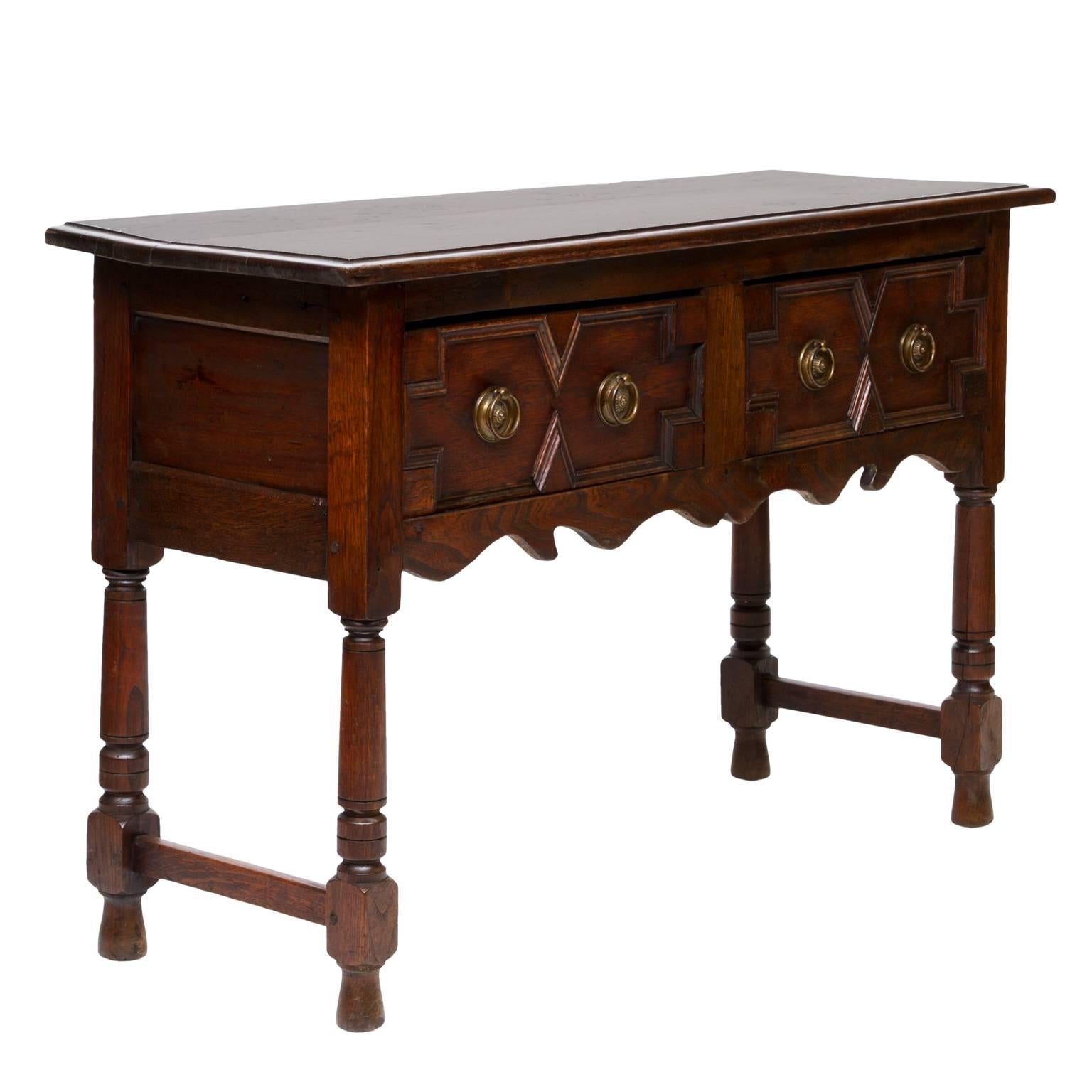 19th century Jacobean oak console table with two drawers. There is a nice two board top, raised panel sides, turned legs joined with stretchers. Notice the geometric patterns to the fronts of the drawers. Thick moldings used to differentiate color