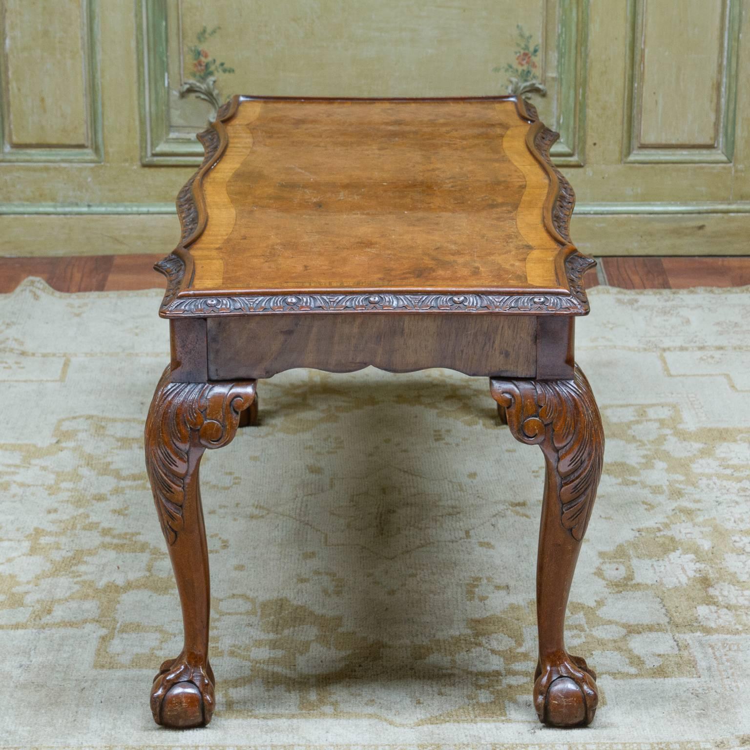 A 1920s English Chippendale walnut and burl walnut cocktail table. Shaped top with carved trim resting on four well carved cabriole legs, ending with a claw and ball foot & carved knees. Can accommodate glass, 1920s.