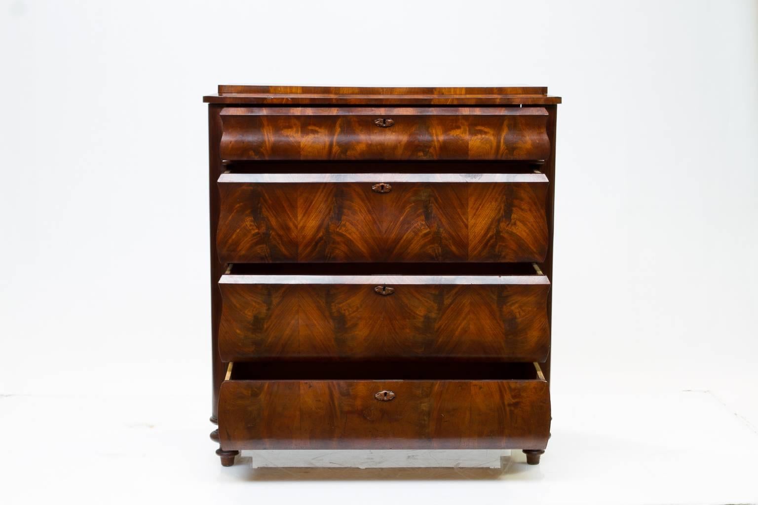 19th century Biedermeier mahogany chest of drawers. Beautiful choice selection of flame mahogany to the drawer fronts which are gracefully curved. Four functional drawers. Unusual tray top then with banded molding accenting the top. Turned feet and