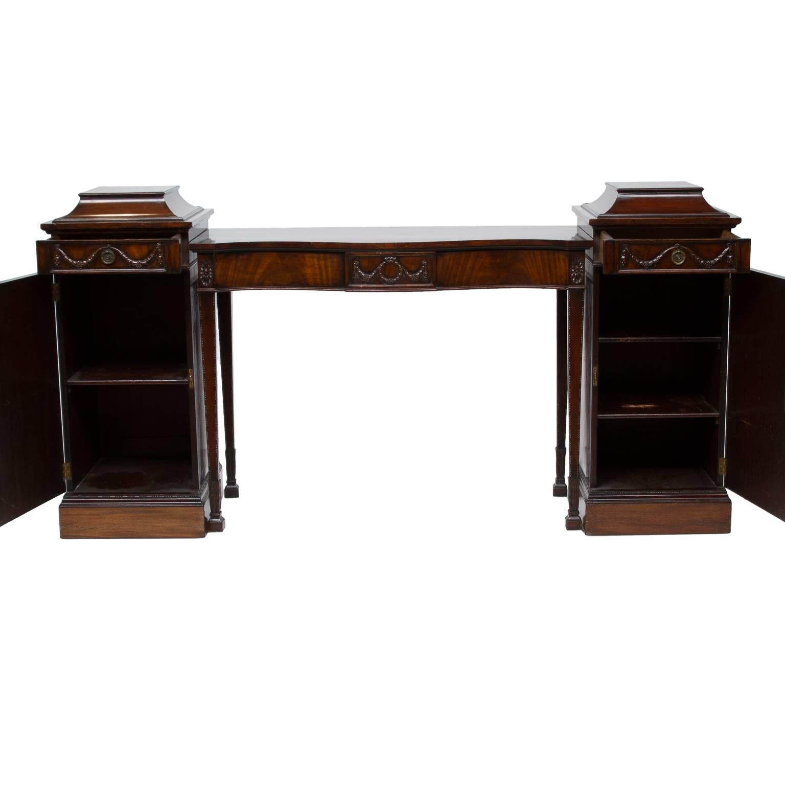 Pedestal base mahogany sideboard in the style of Scottish neoclassical architect Robert Adams, with carved swags and rosettes. Features four drawers and two cabinets. Interior cabinet has one shelves. The piece separates to reveal a console in