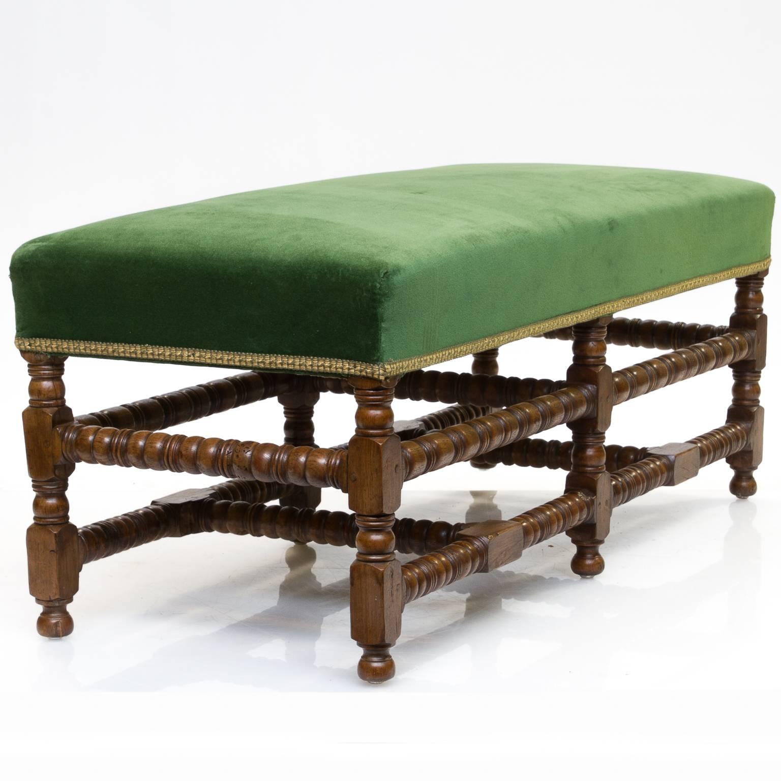 An English oak bench with a fine turned base. Very sturdy especially with the legs and stretchers support. Larger in scale comfortable for two individuals. A green velvet covering in very good condition or can be recover inexpensively. There are peg