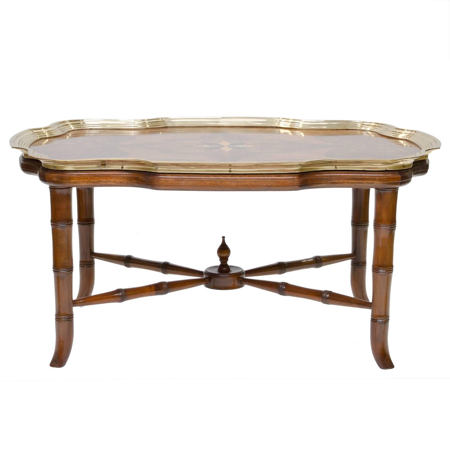 An impressive coffee table which is large in scale vs an usual tray table. This table has a stunning veneered top with an inlaid starburst. There is a shaped top and the brass edging mimics the shape. The base was made for the top. Solid mahogany
