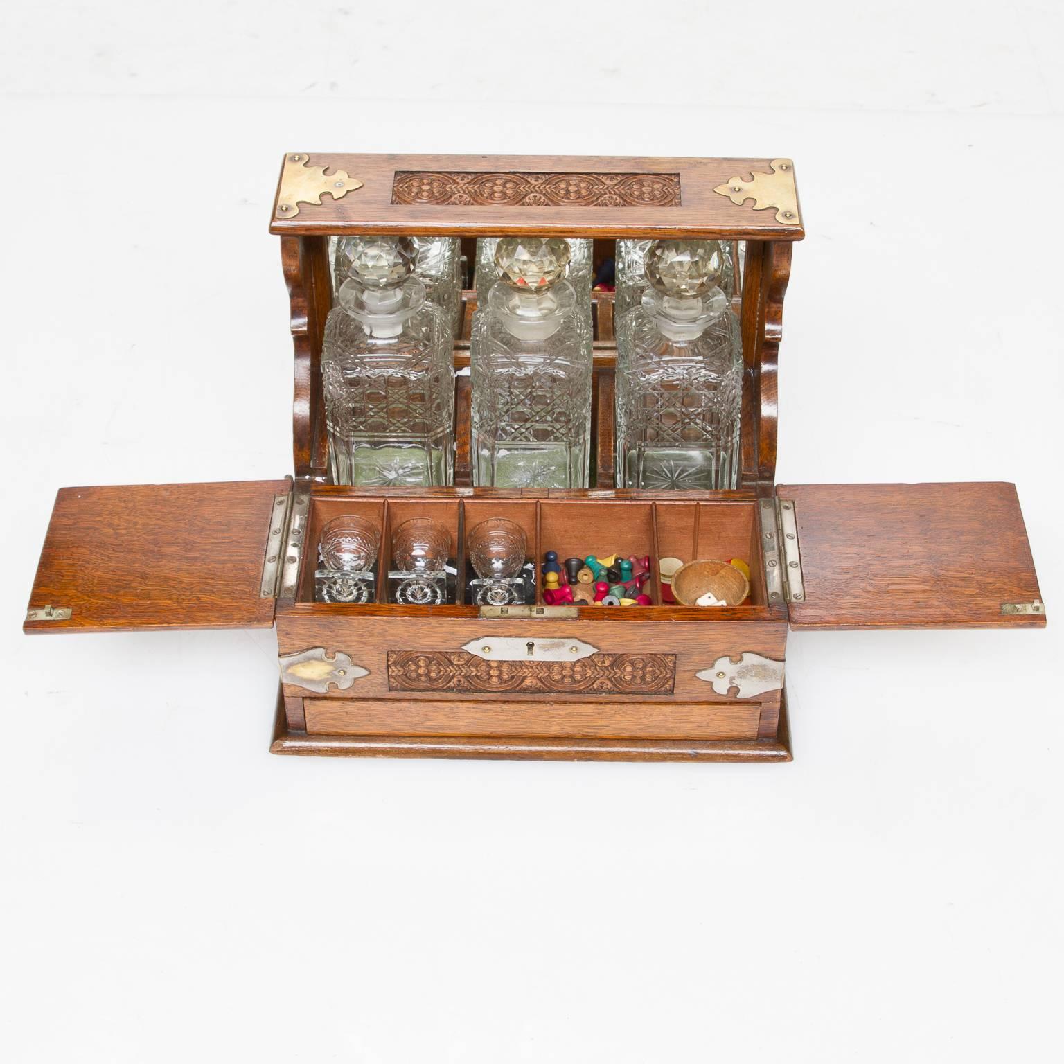 A very nice quality English oak carved decanter set and case fitted interior with a release button revealing a card drawer. Very well carved and handsome brass mounts.