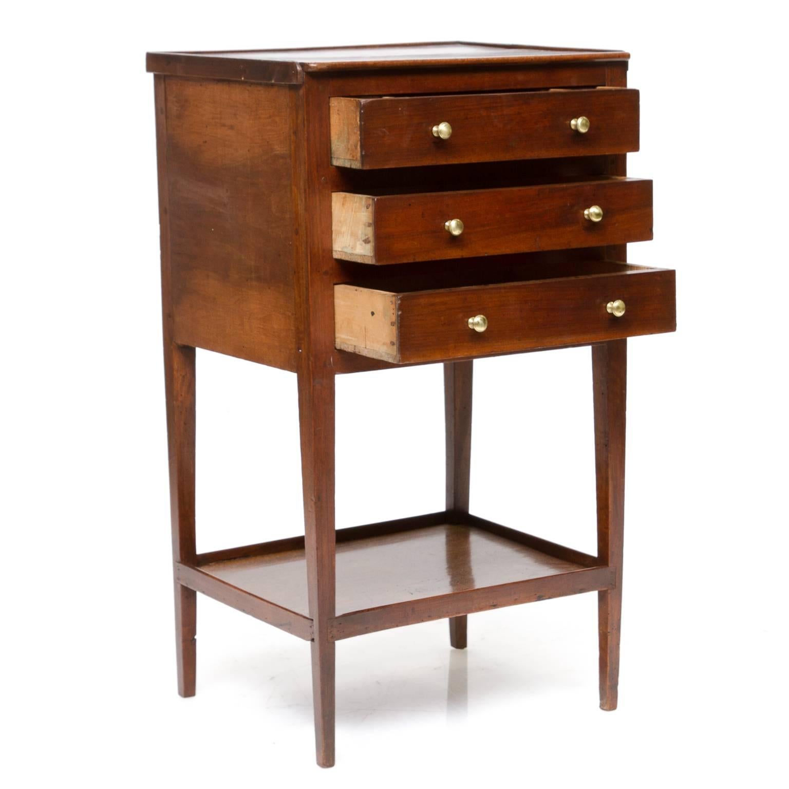 A wonderful 19th century French Provincial walnut side table with three drawers (these slide very well), each with two brass pulls. The top has trim on three sides which are slightly raised. Four tapered legs connected with a lower shelf giving