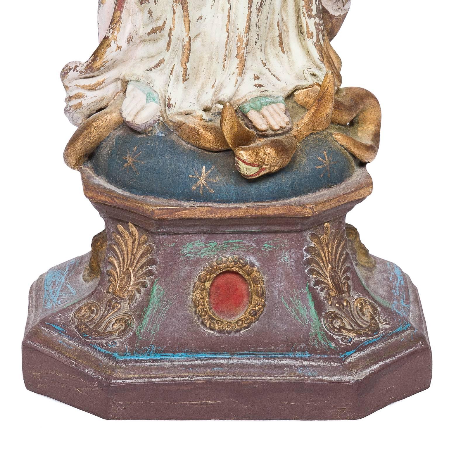 A decorative sculpture of the Virgin Mary. Papier mâché painted to look old, cream body and muted mat paint colors along with gold paint and complete with a pearl earring hanging. There is a mounted metal headdress which has gilt paint.