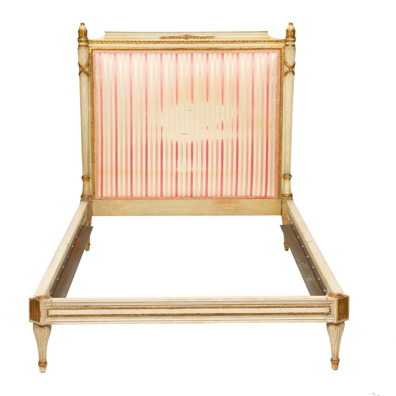 A pair of Louis XVI painted twin beds with a striped fabric. Original painted frame with ornamentation. The ornamentation is highlighted with gold leafing. There is a bead moulding framing the back upholstered headboard as well accenting the side