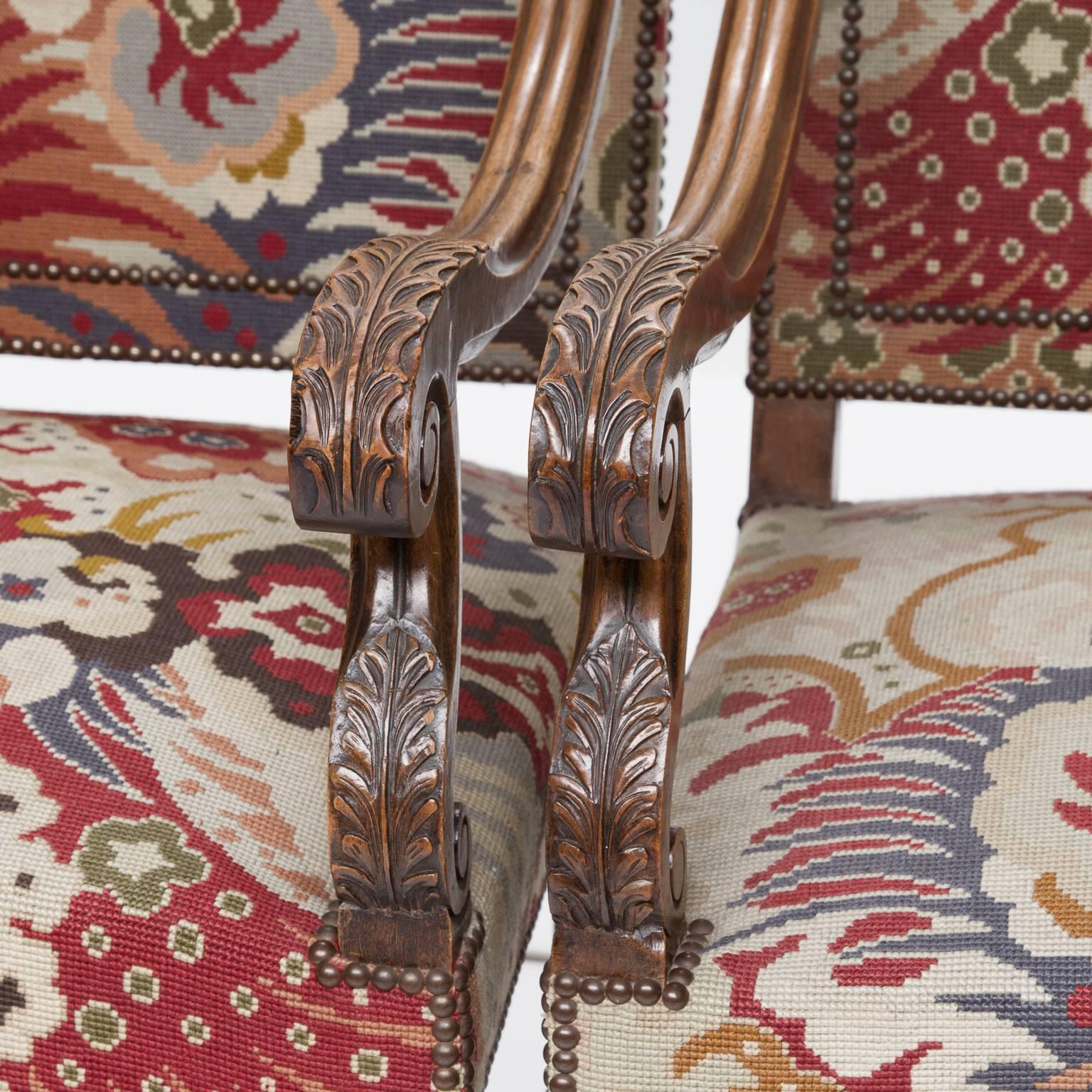 A large pair of walnut Louis XIV style tapestry armchairs from the late 19th century. The backs are shaped with brass nailheads which match the serpentine top of the chairs. Wonderful carved and scrolled armsupports and armrest which are repeated